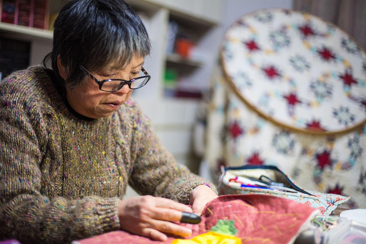 一位年长妇女在她的家中缝纫和制作工艺品