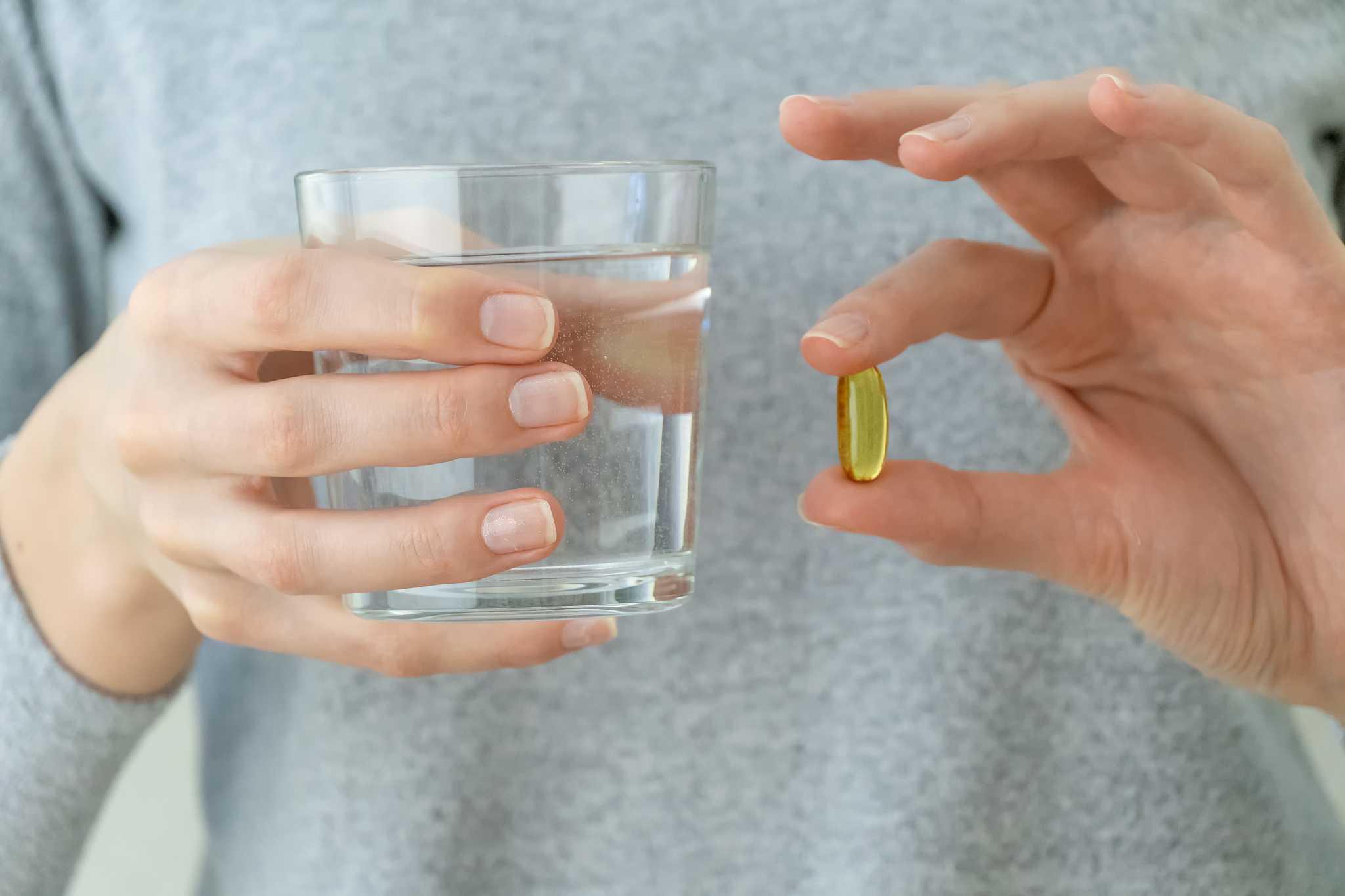 woman in a gray jacket is holding an omega-3 fish oil capsule an