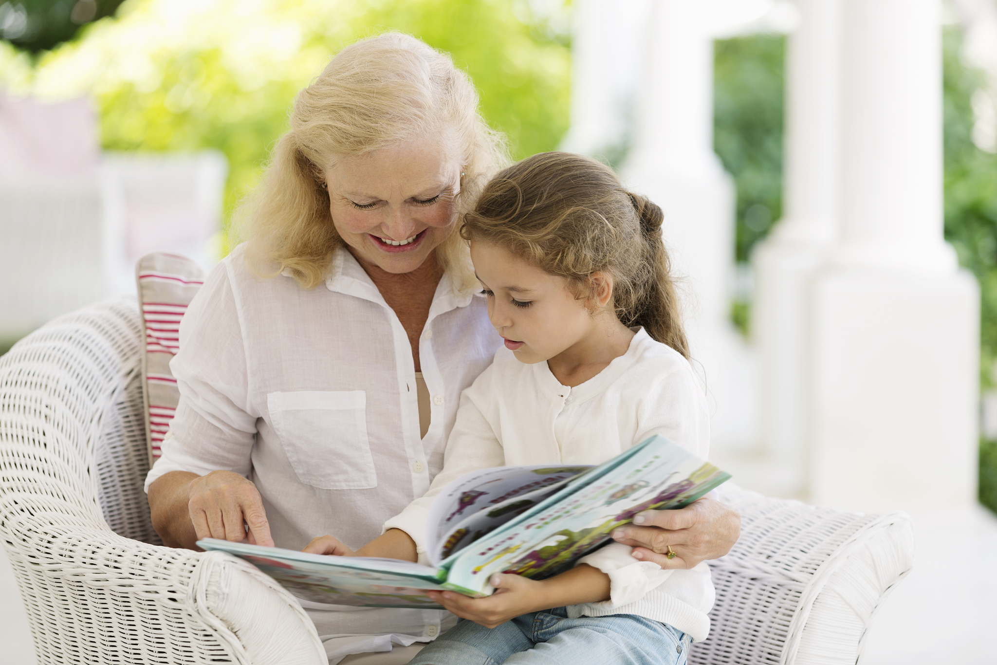 older woman reading to granddaughter on porch