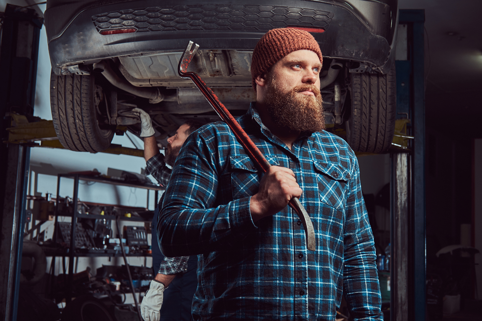 two bearded brutal mechanics repair a car on a lift in the garag