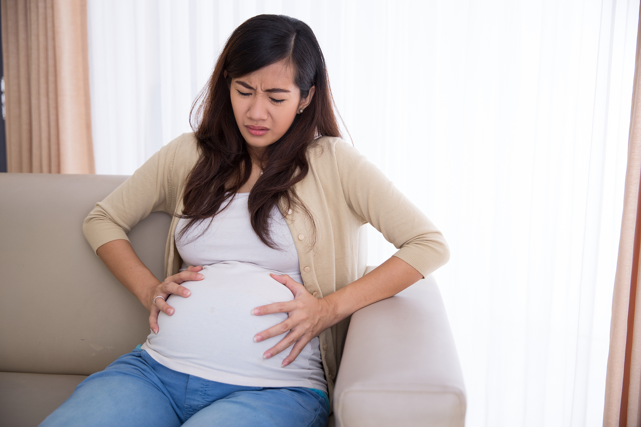asian pregnant woman has stomachache sitting on her couch