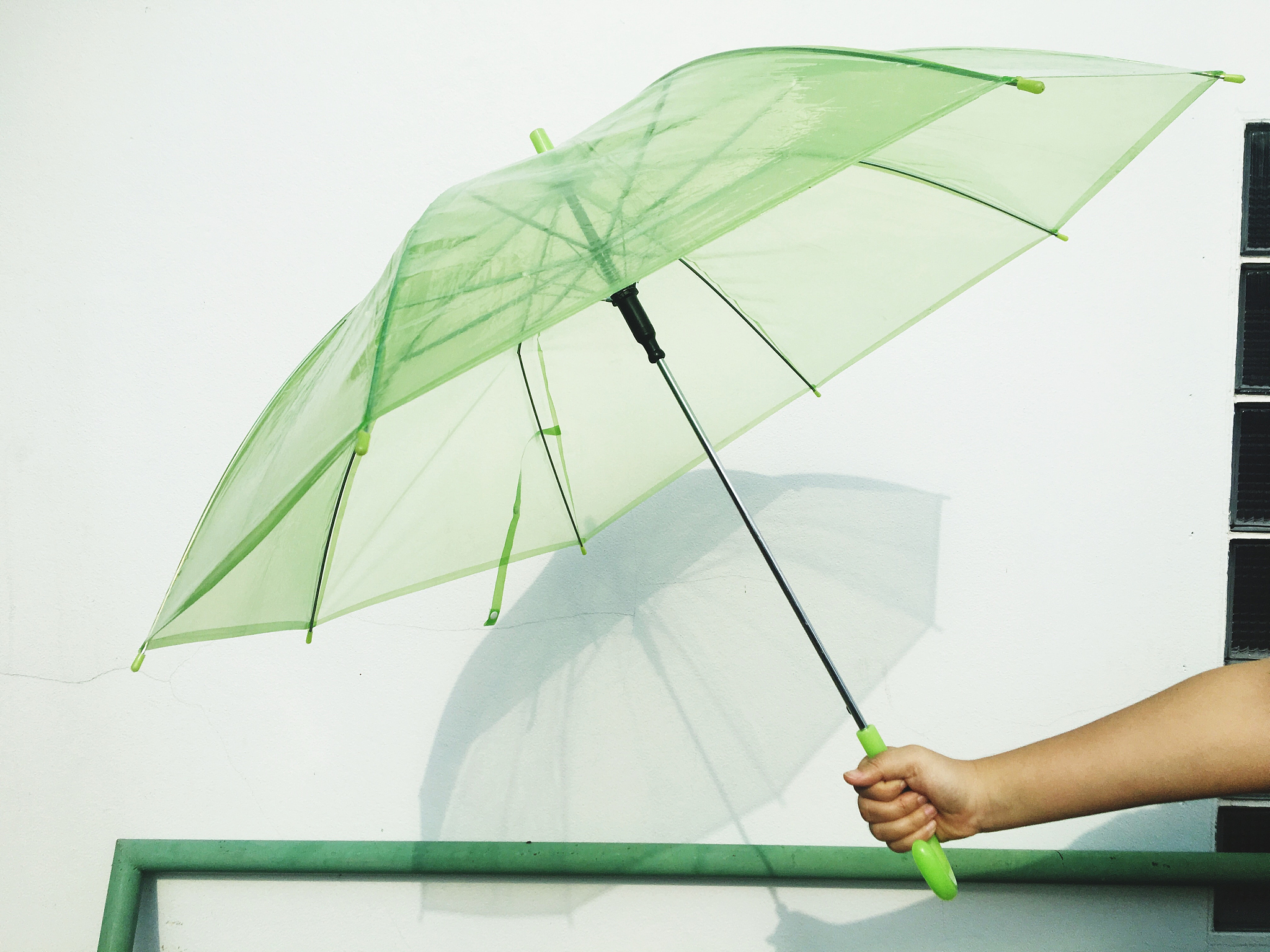 midsection of woman holding green umbrella by white wall
