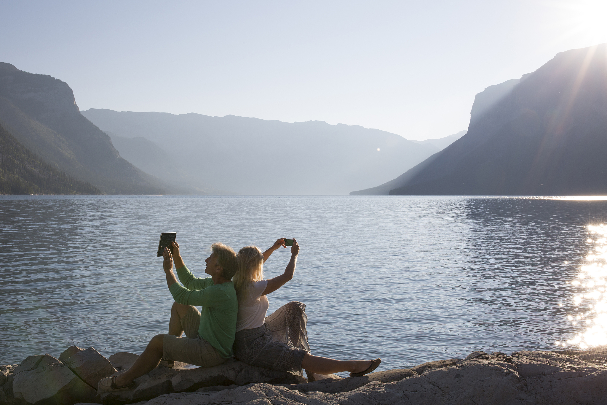 couple taking pics of  lake with phone and tablet