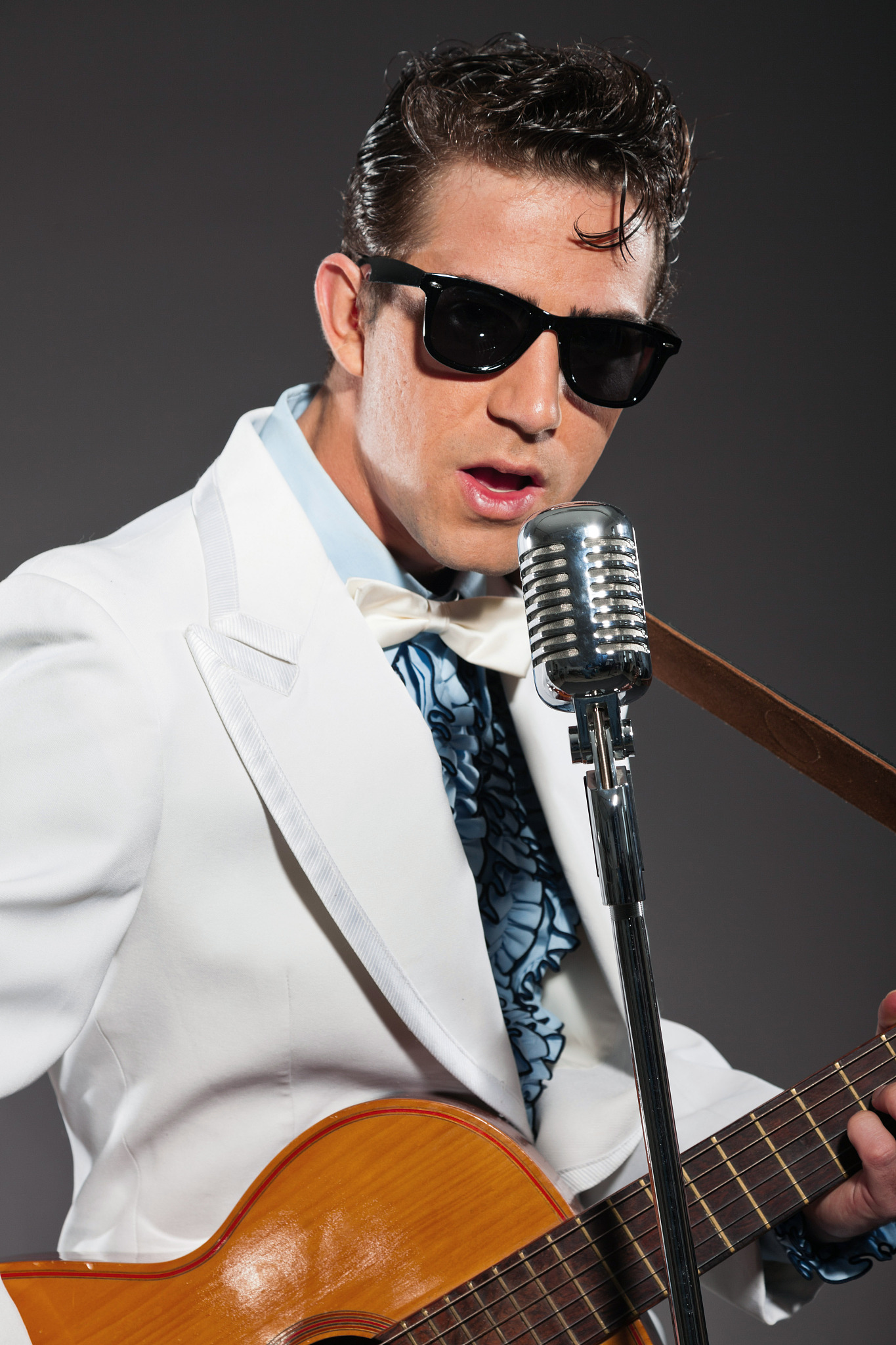 retro rock and roll singer with guitar wearing white suit.