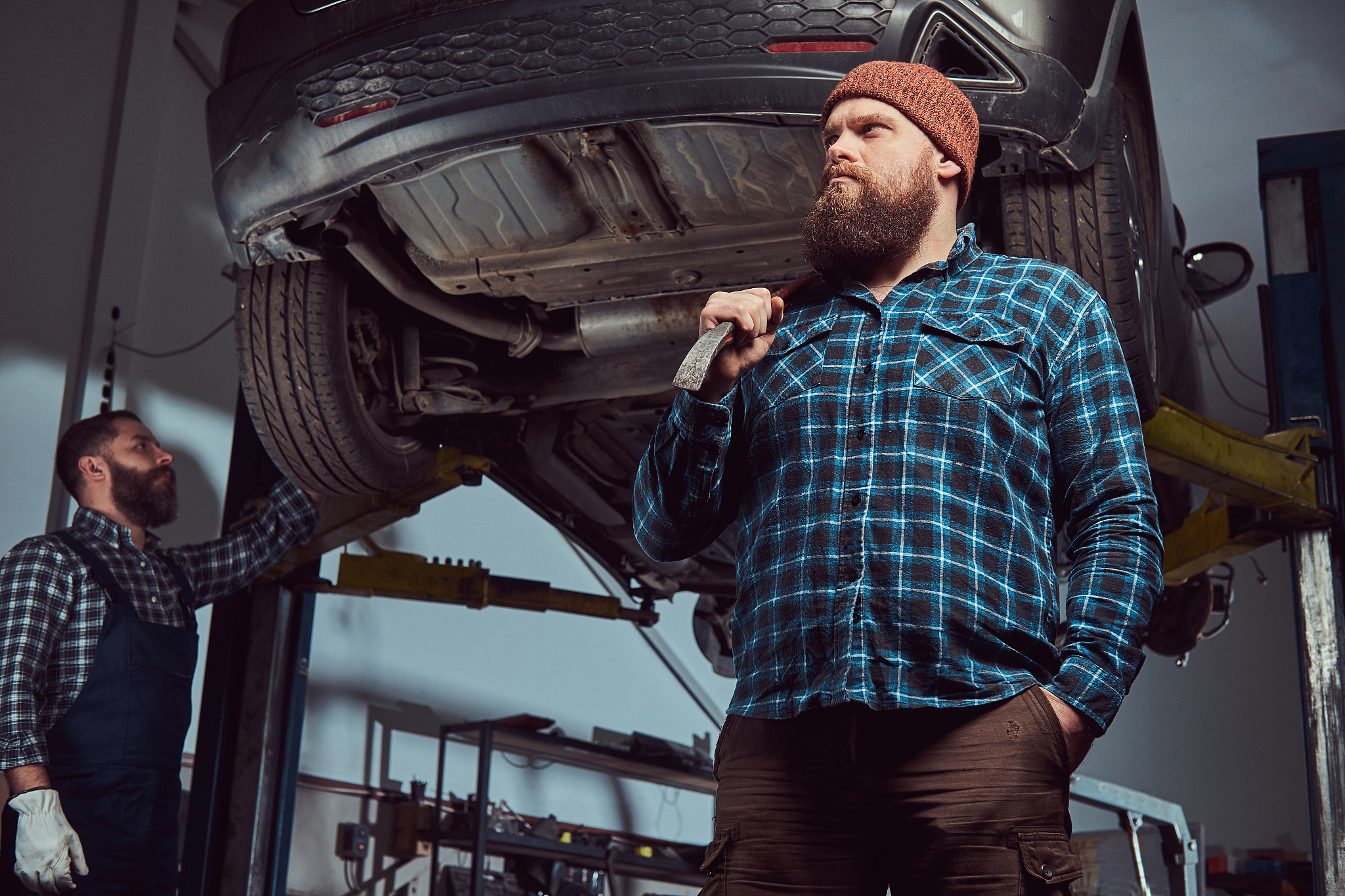 two bearded brutal mechanics repair a car on a lift in a garage.