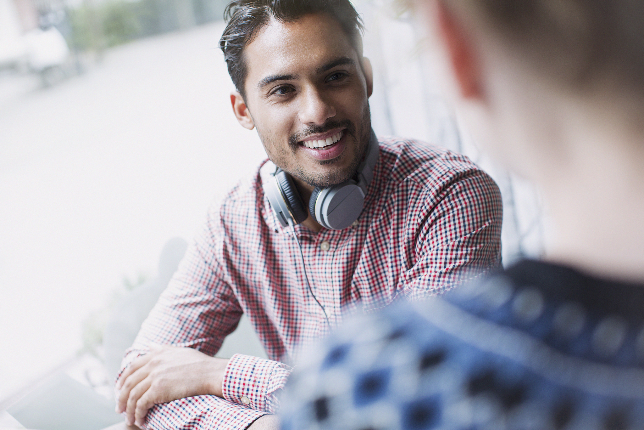smiling young man with headphones talking to window at cafe wind