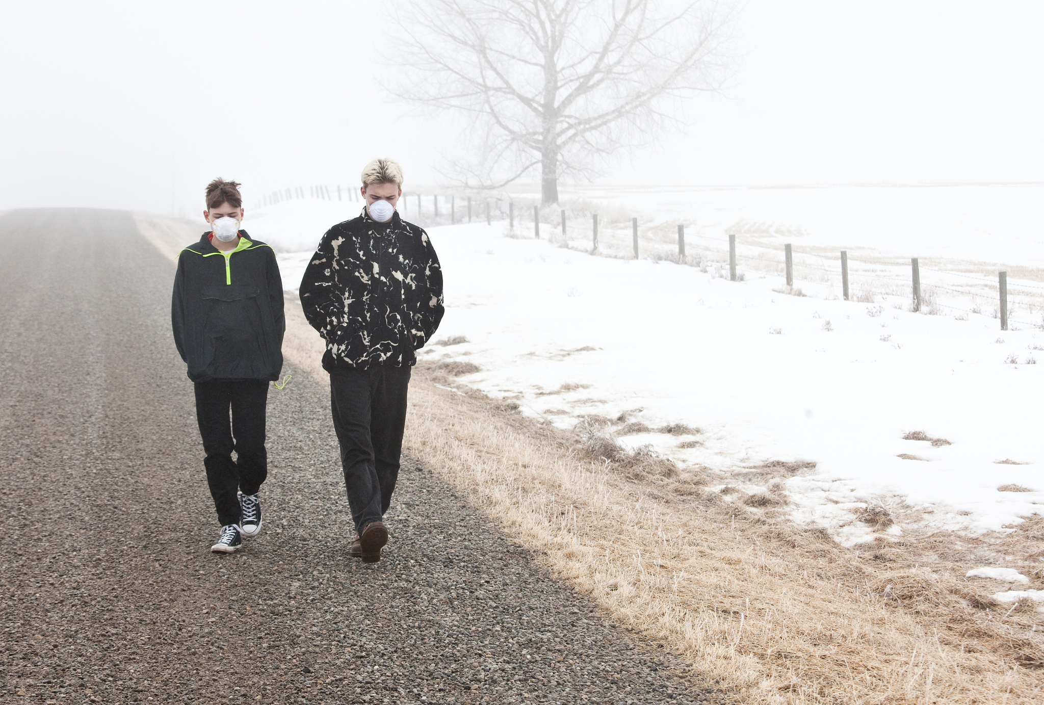 two caucasian boys walking down a foggy rural road with face mas