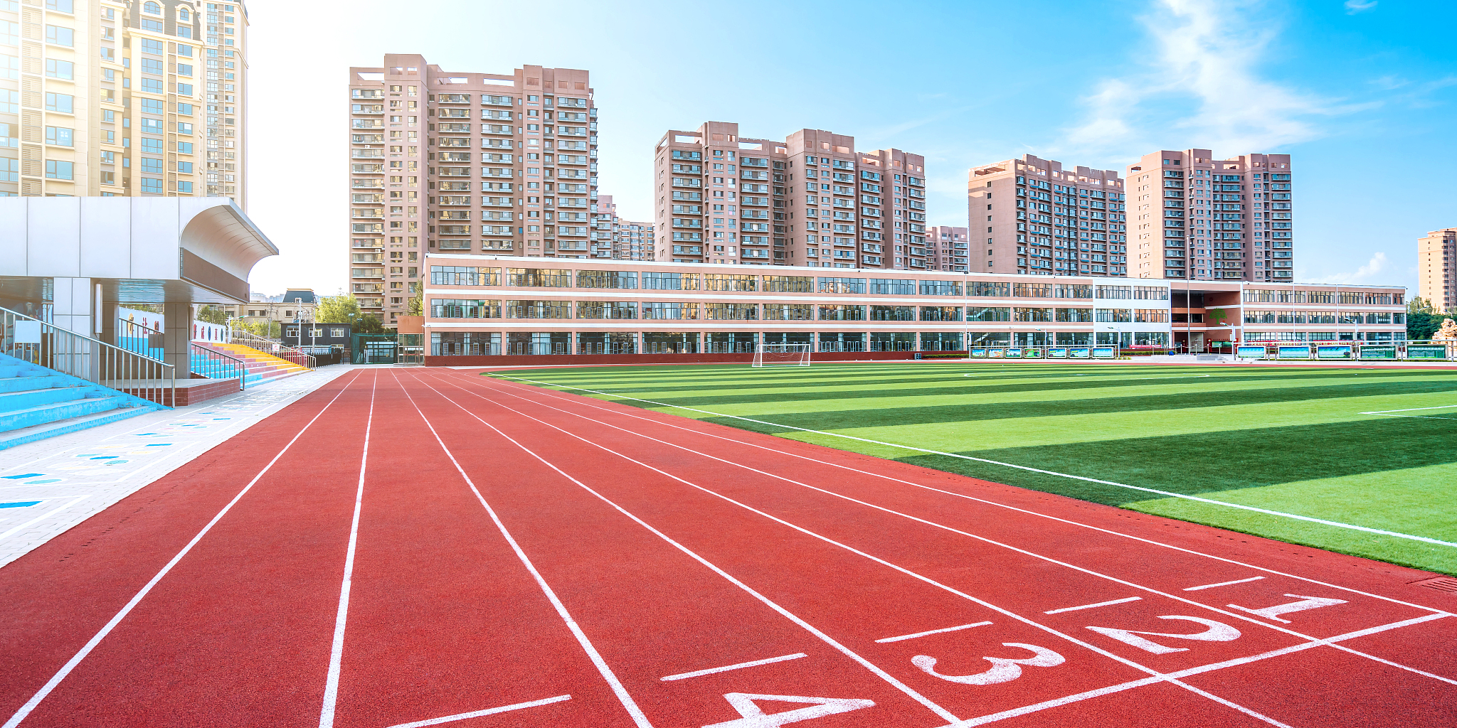 阳光下的体育场红色跑道和远处的高楼建筑