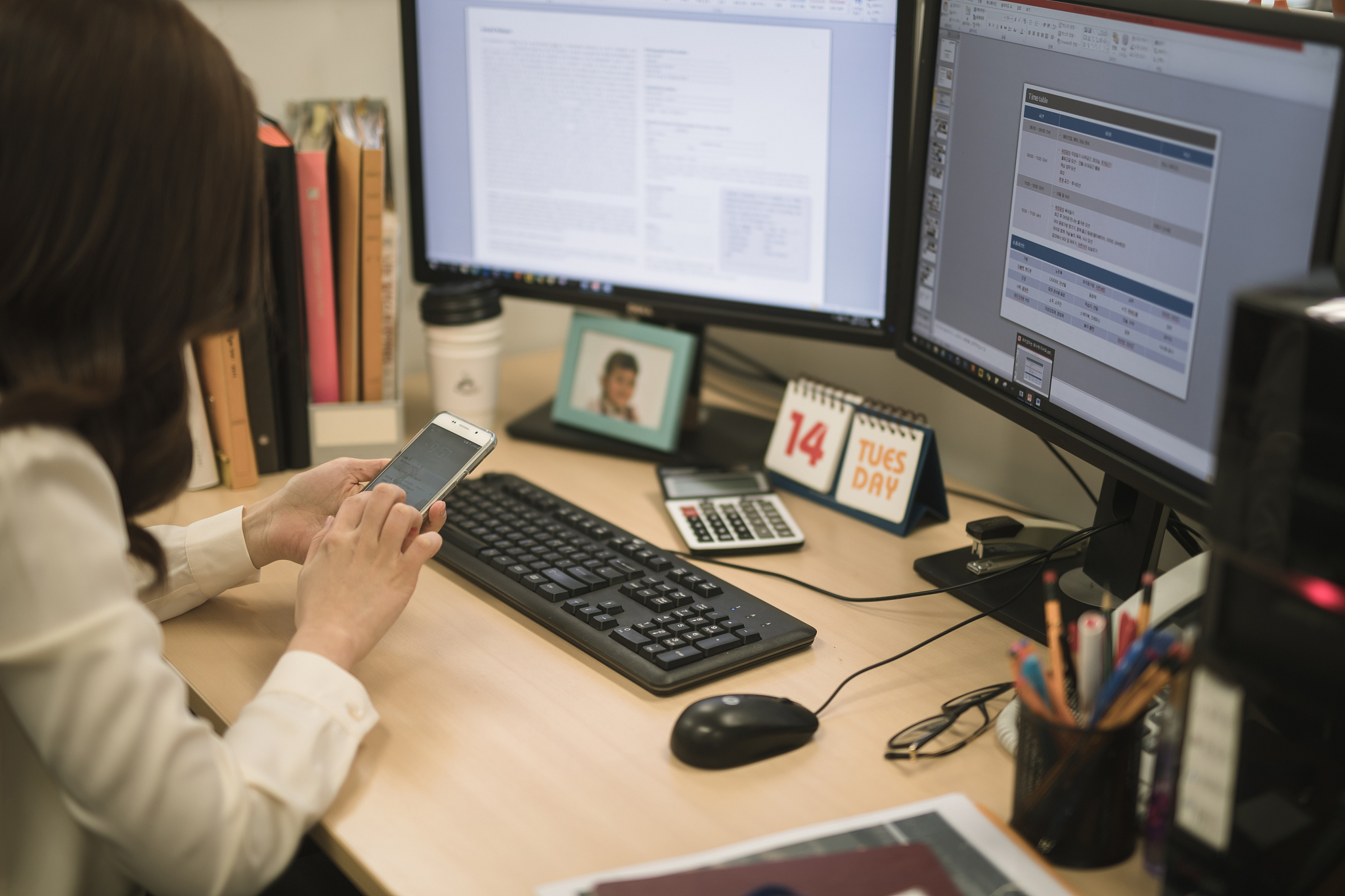 photography of businesswoman sitting by desk looking at smartpho