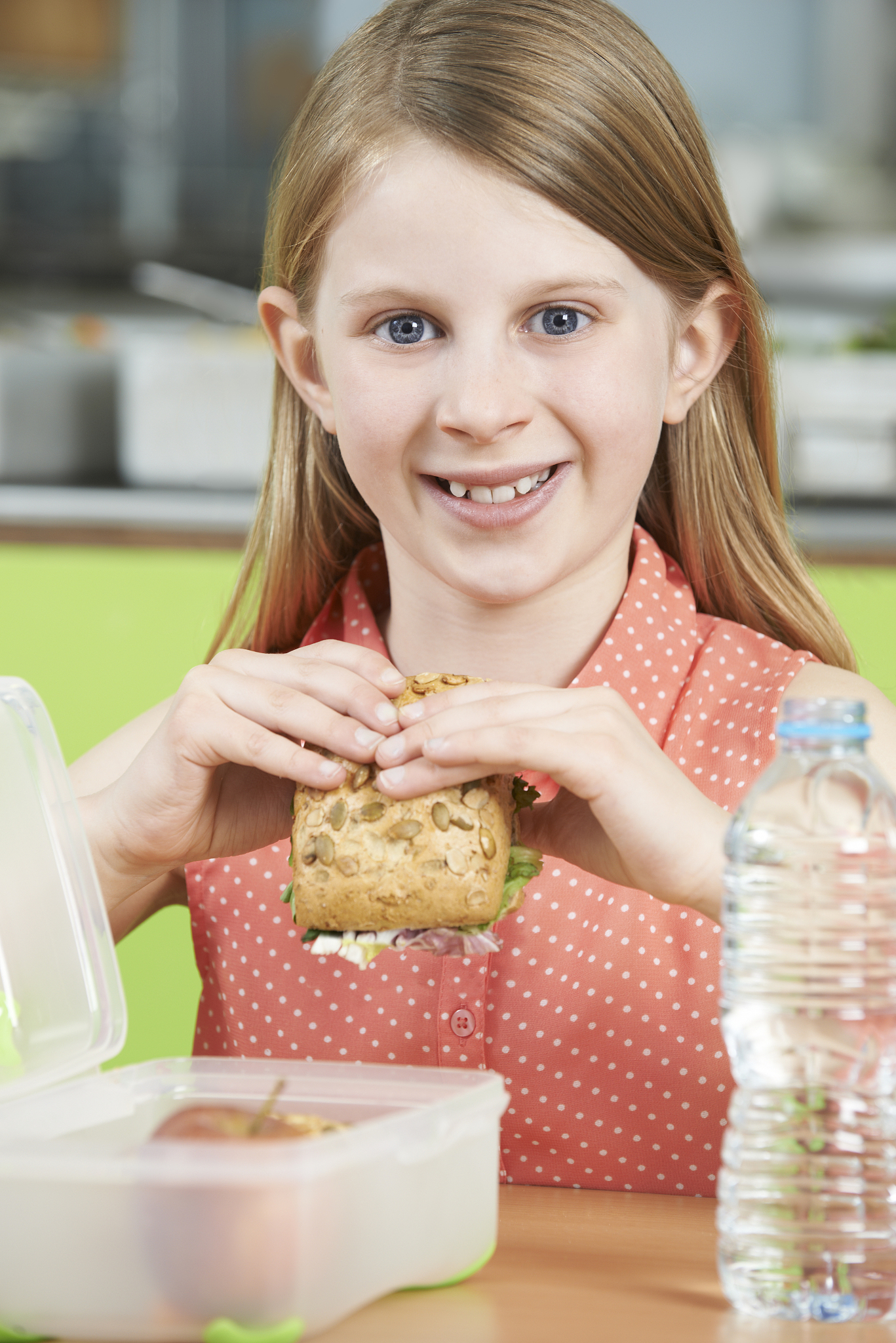 female pupil sitting at table in school cafeteria eating healthy