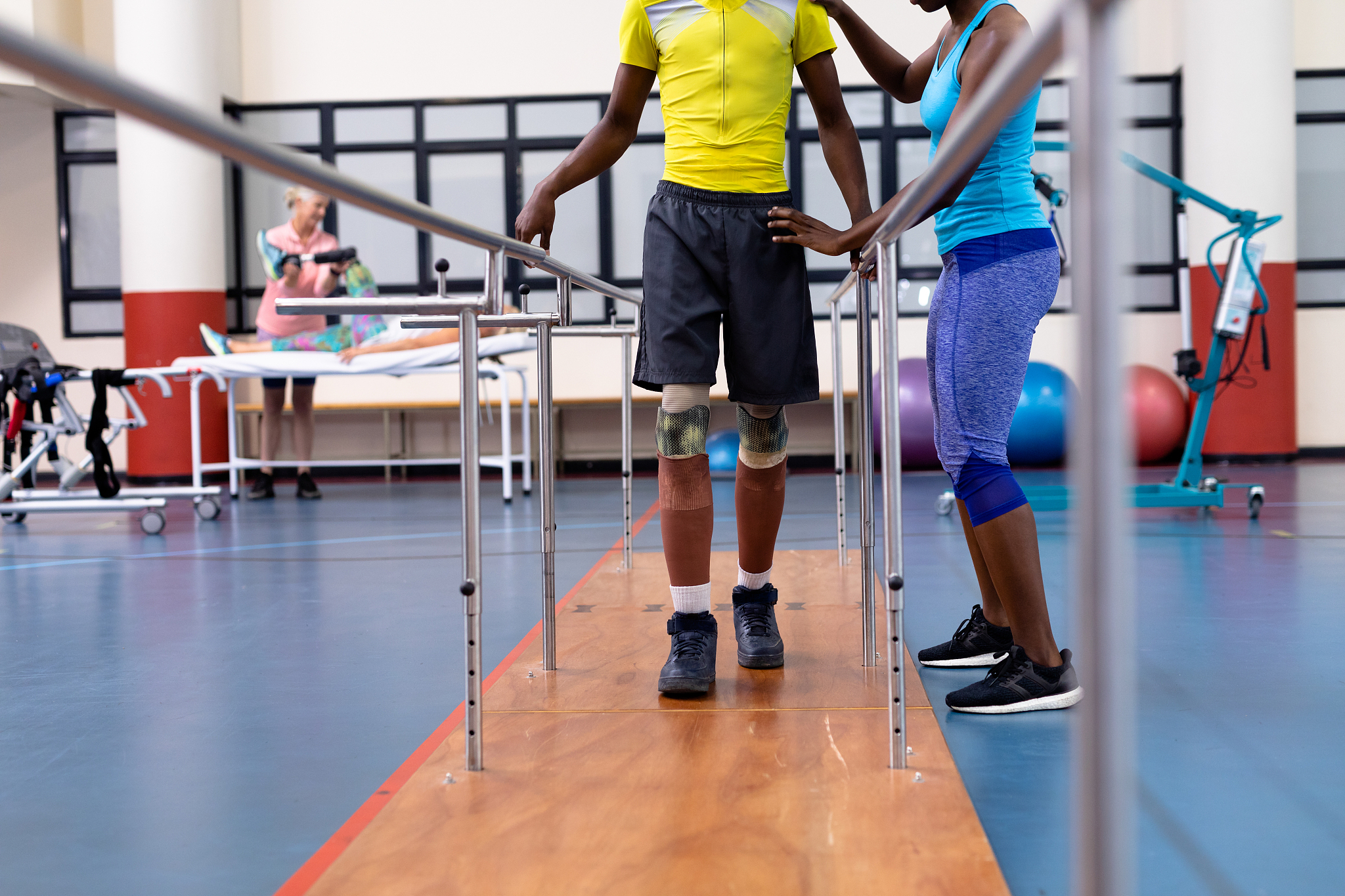 physiotherapist helping disabled man walk with parallel bars in 