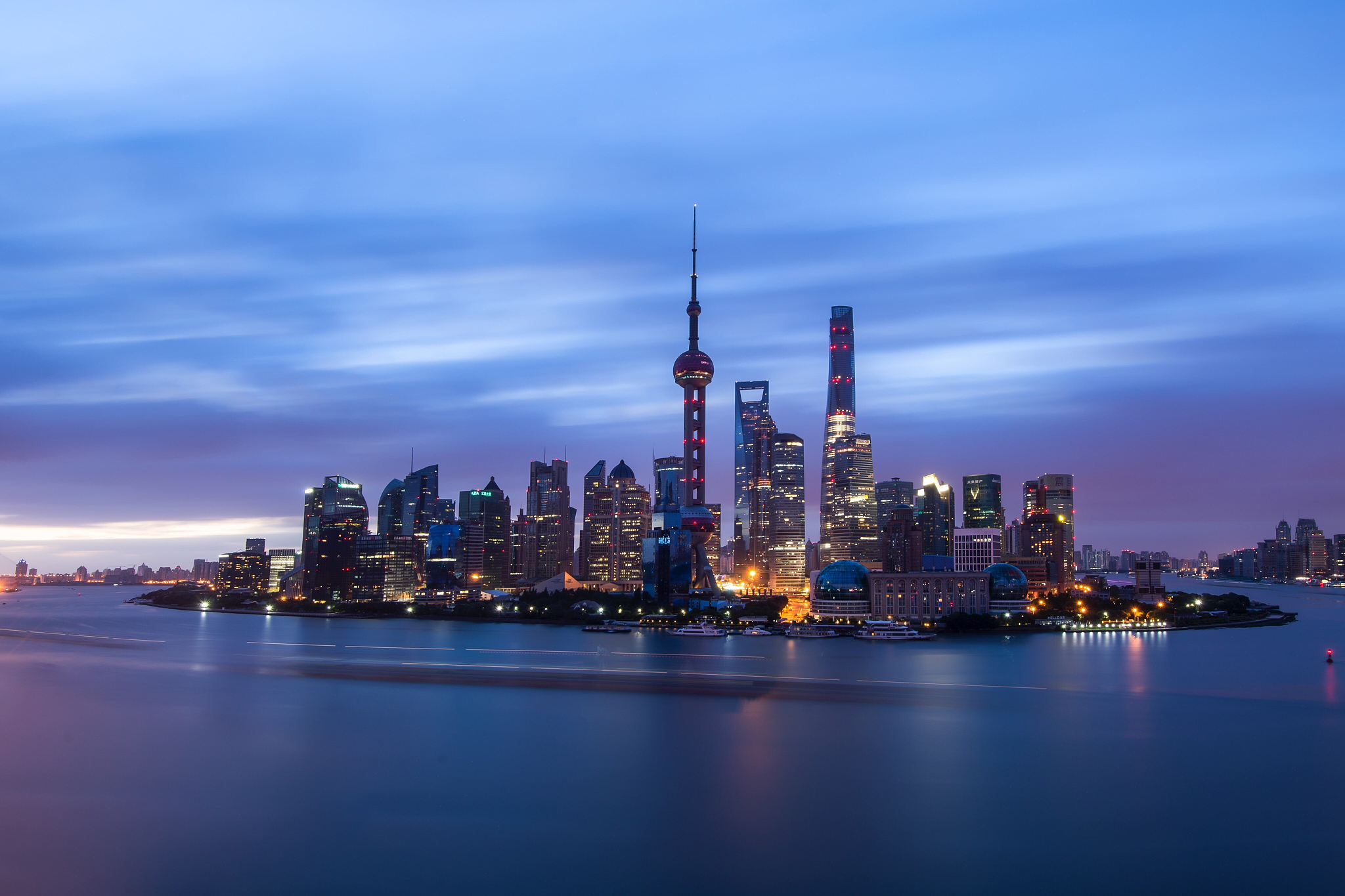 illuminated city by sea against sky at sunset