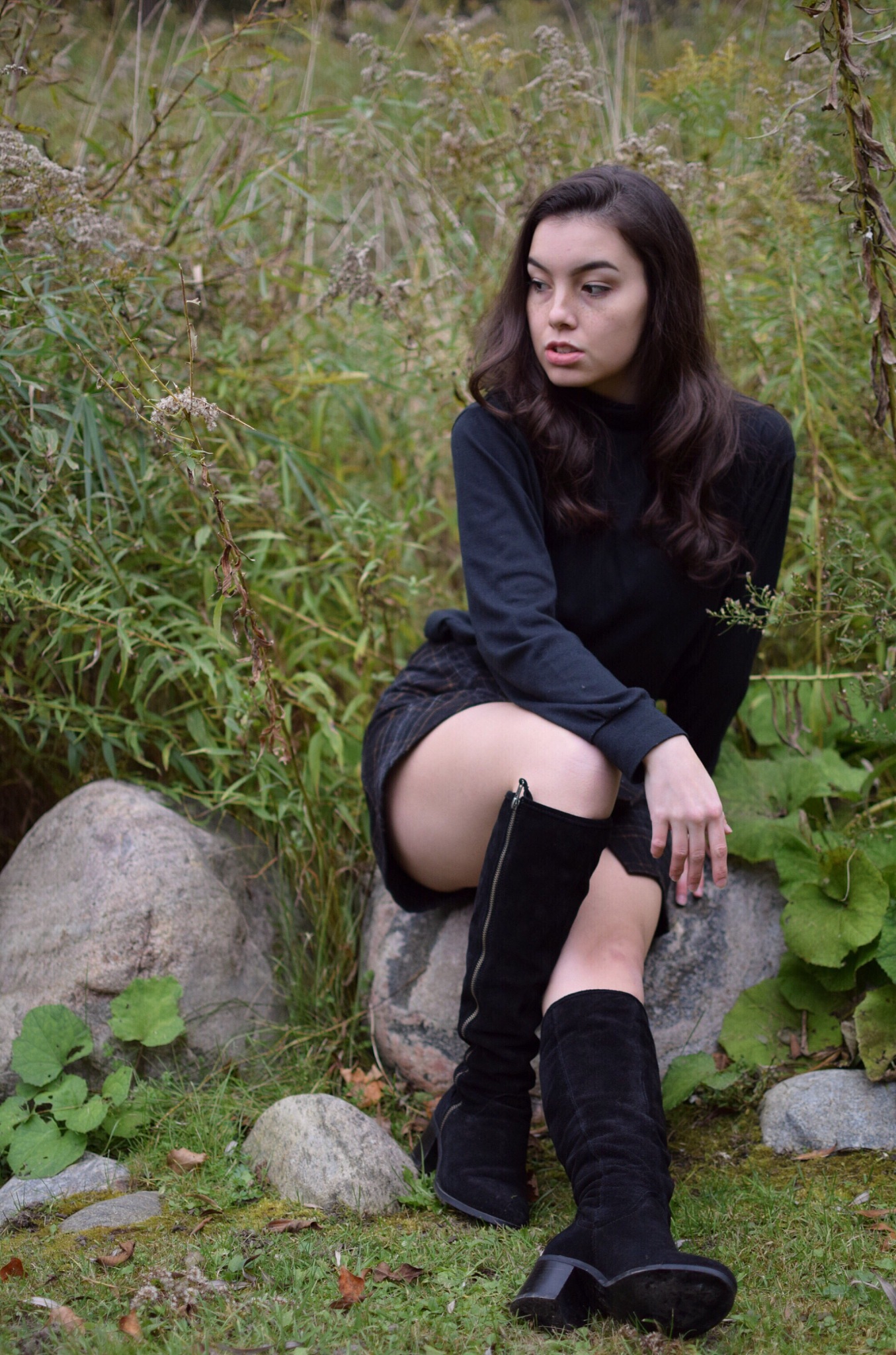 young woman looking away while sitting on rock against plants