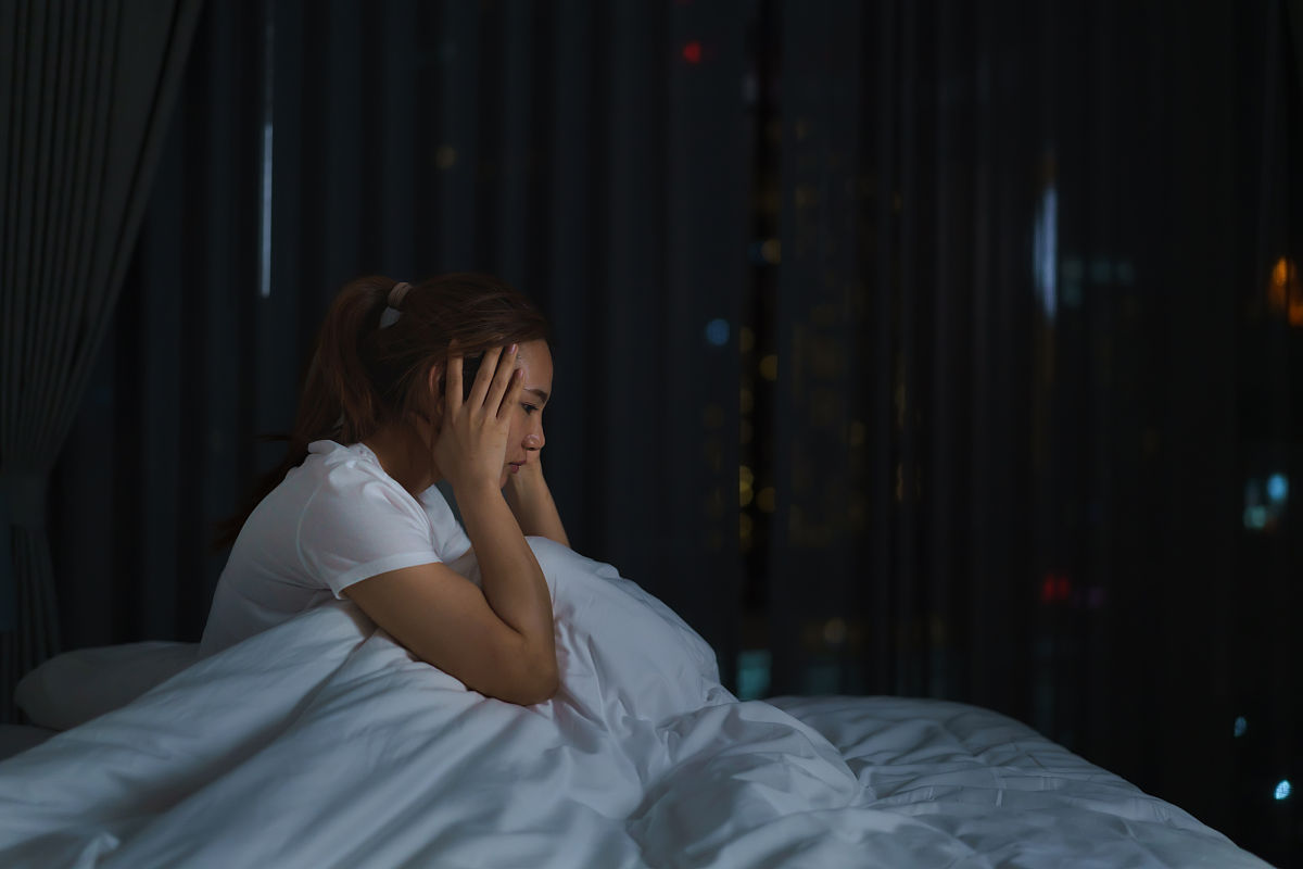 亚洲妇女躺在白色的床上在卧室里看起来担心或思考一些关于她的生活或