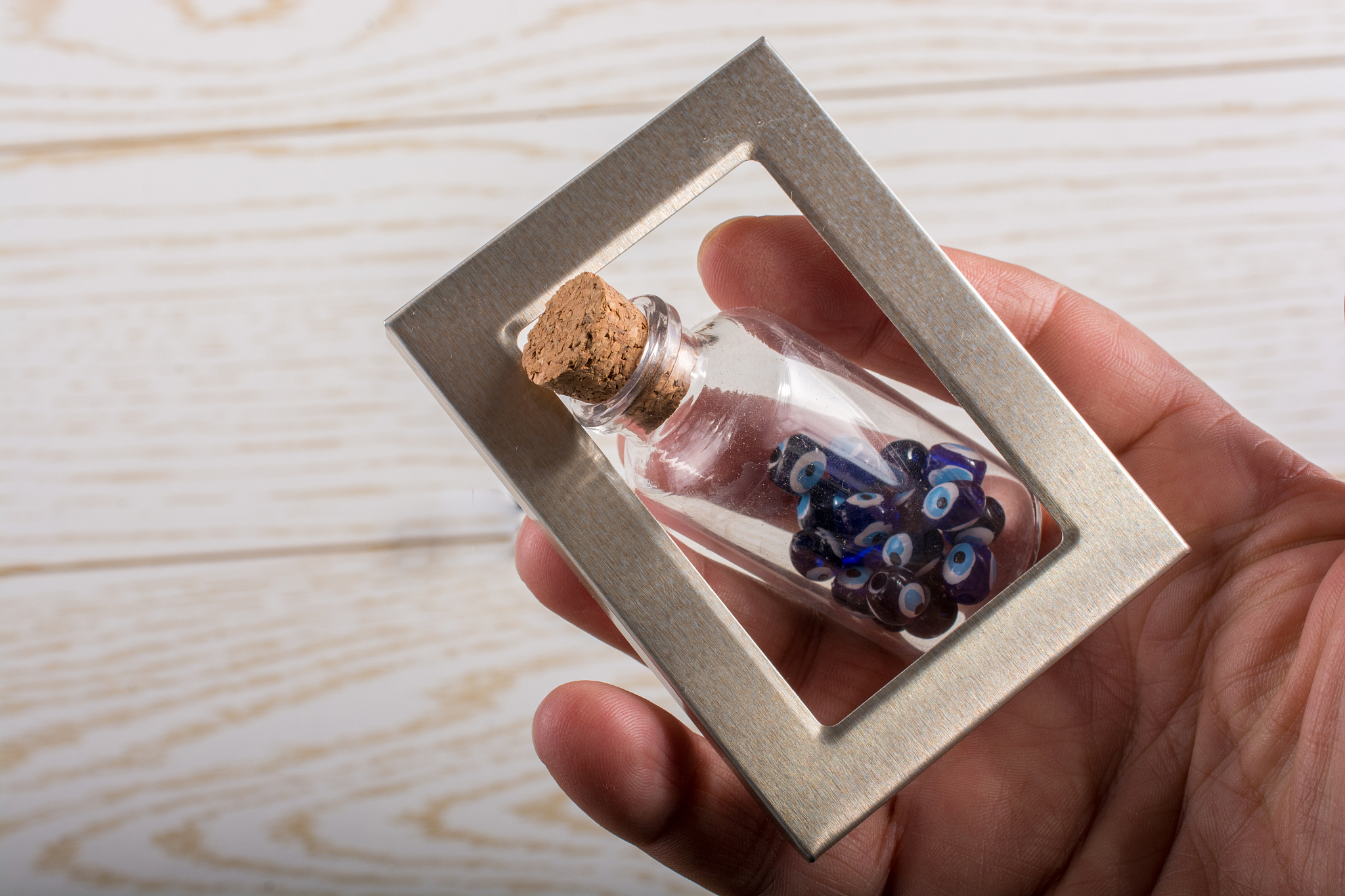 close-up of hand holding beads in bottle with frame on table