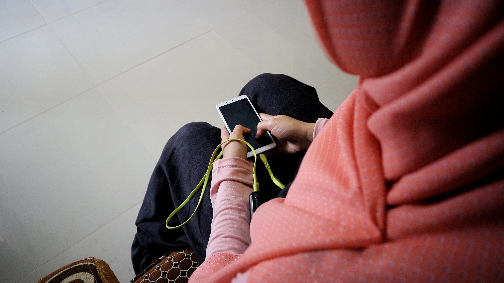 hijab woman is sitting holding a cellphone that is being charged