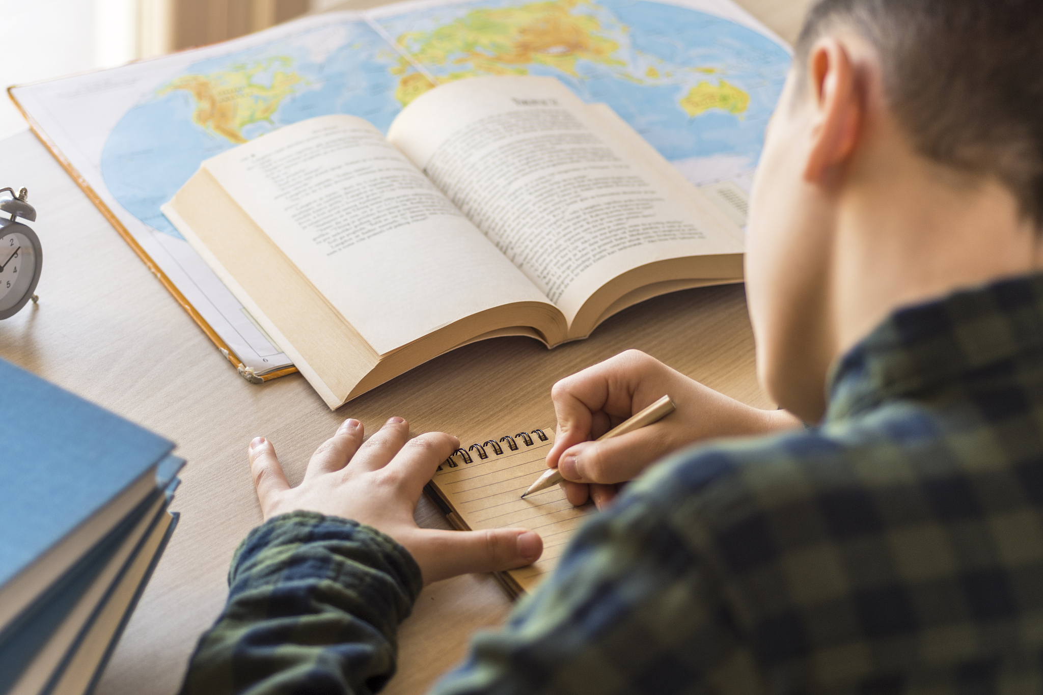 young schoolboy writing on notebook and studying on desk