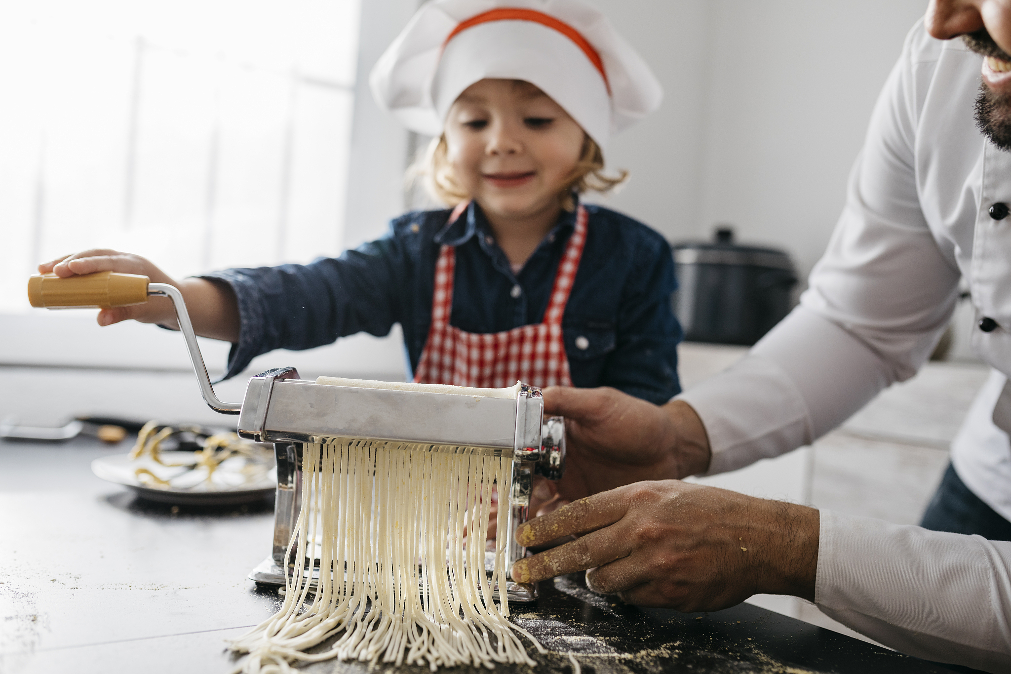 father and daughter making homemade pasta with pasta machine in 