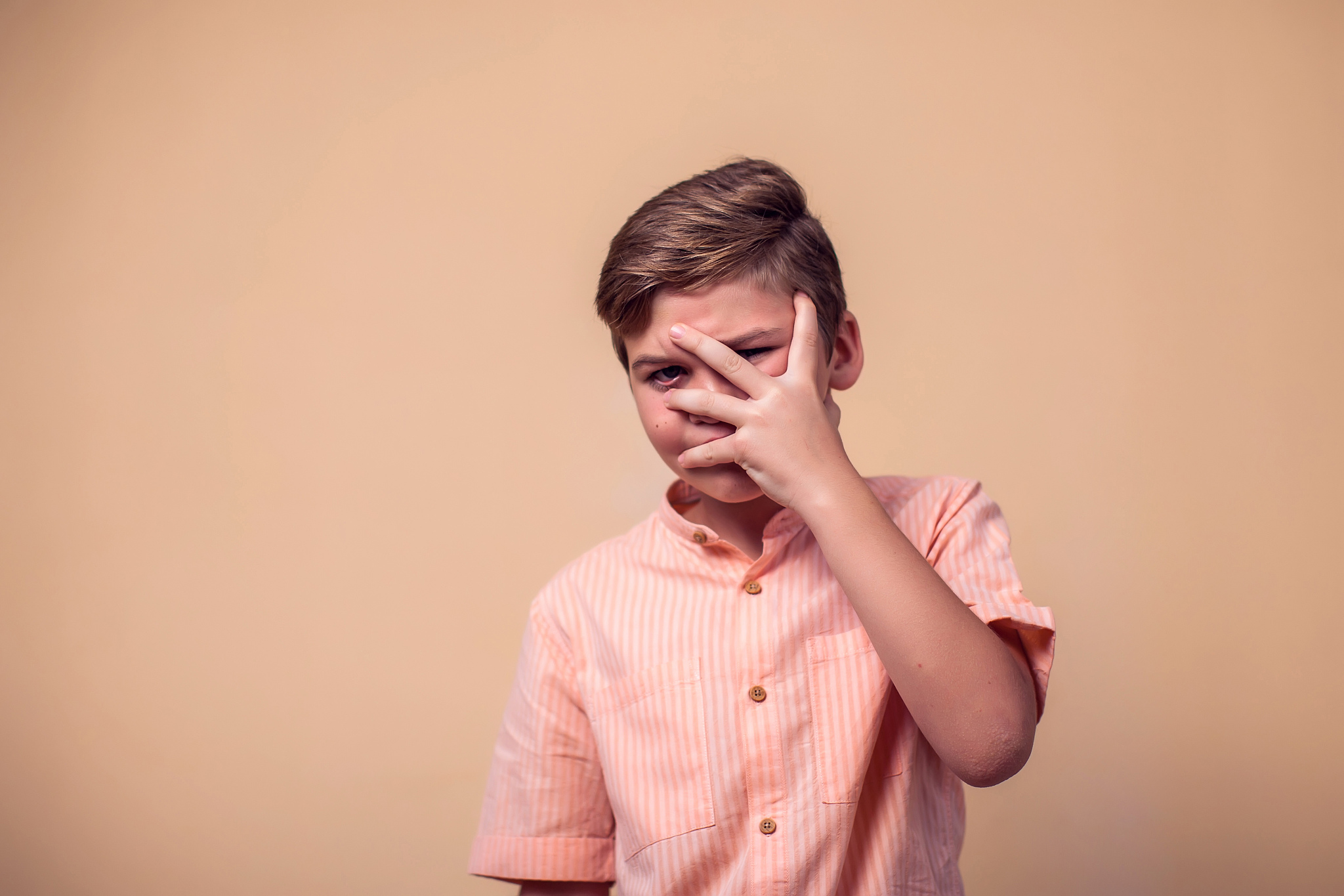 a portrait of afraid kid boy covering his face with hand. childr