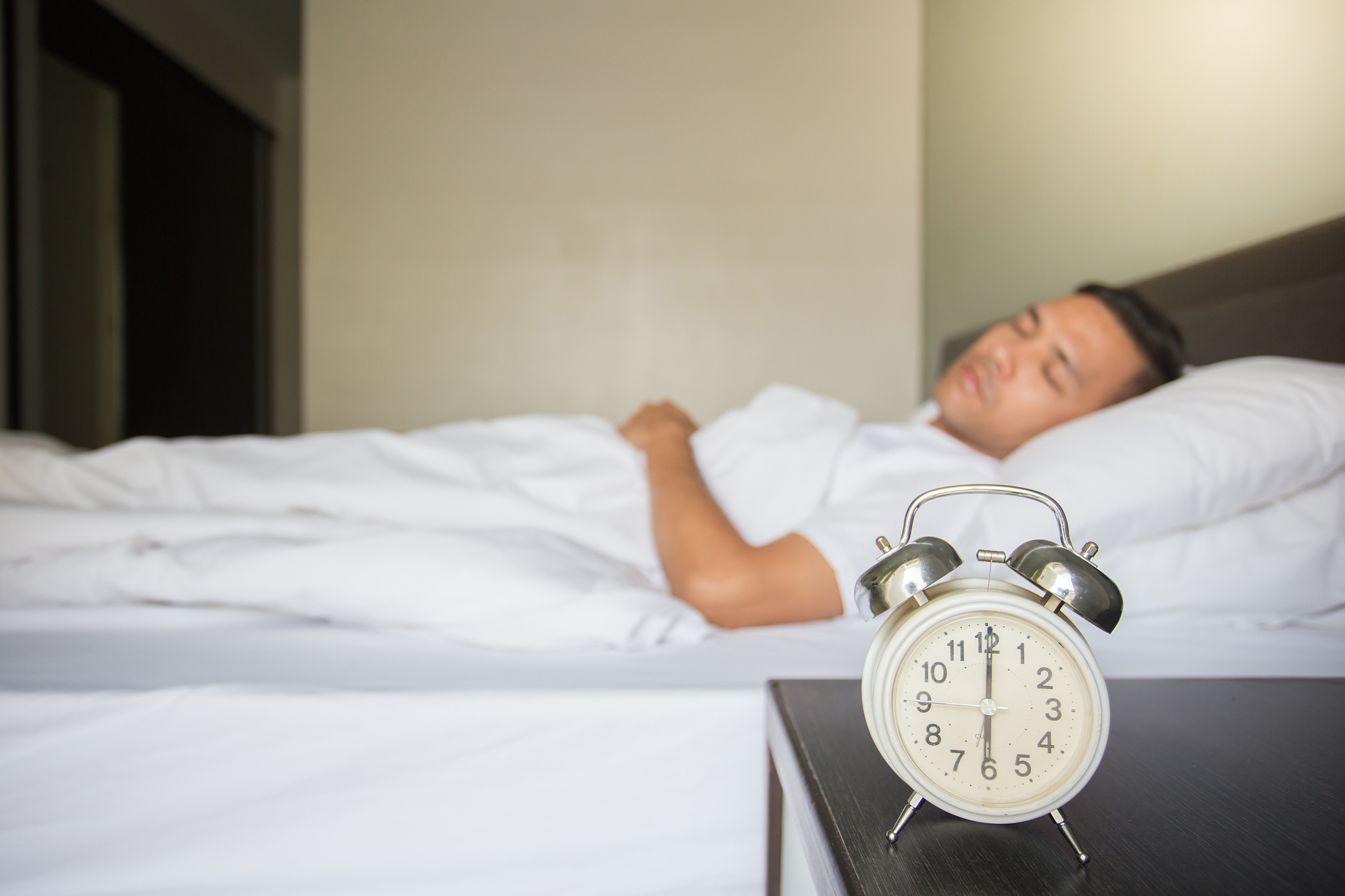 man sleeping on bed by alarm clock at night table in bedroom