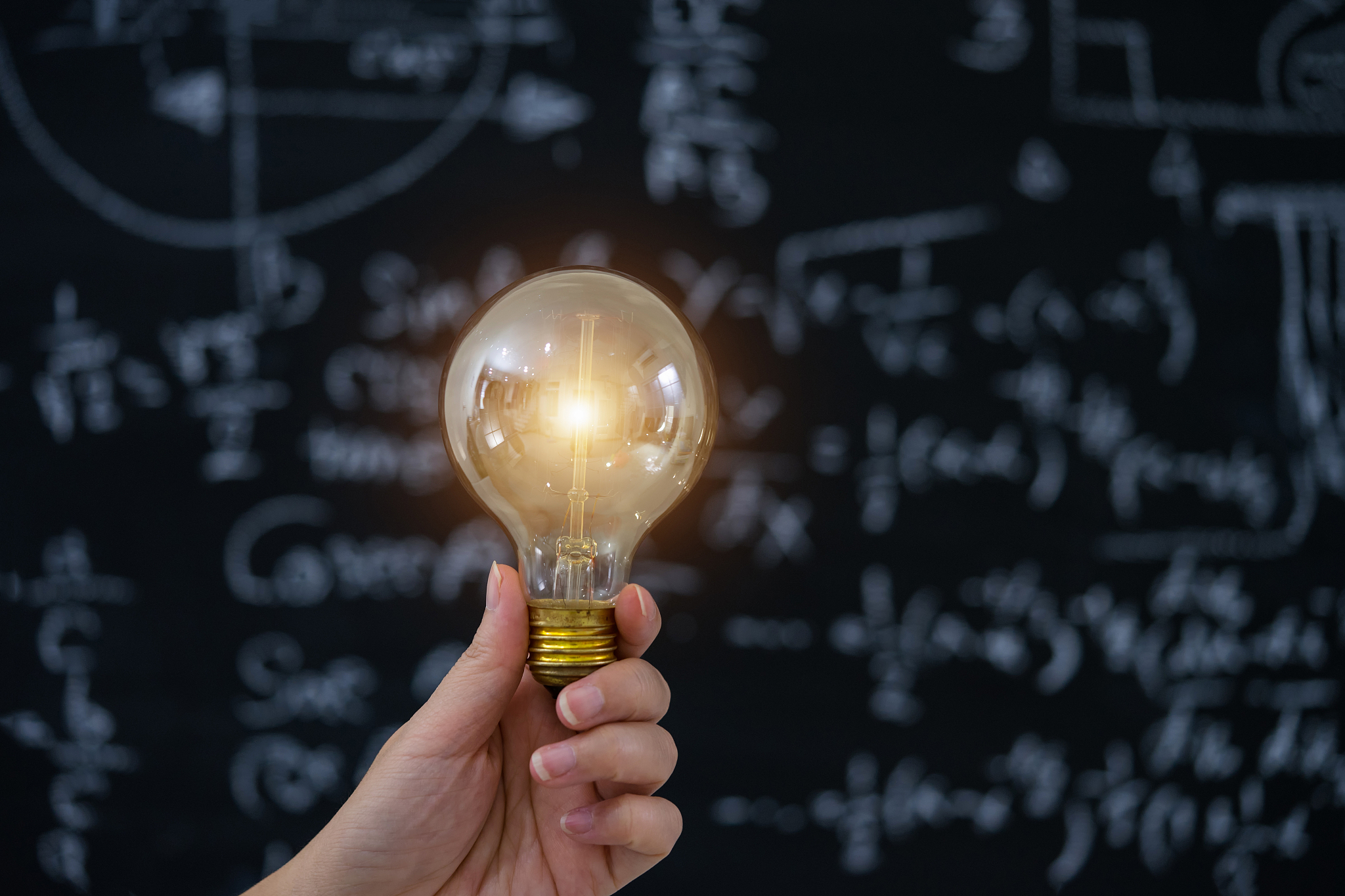 hand holding light bulb on blackboard background.
