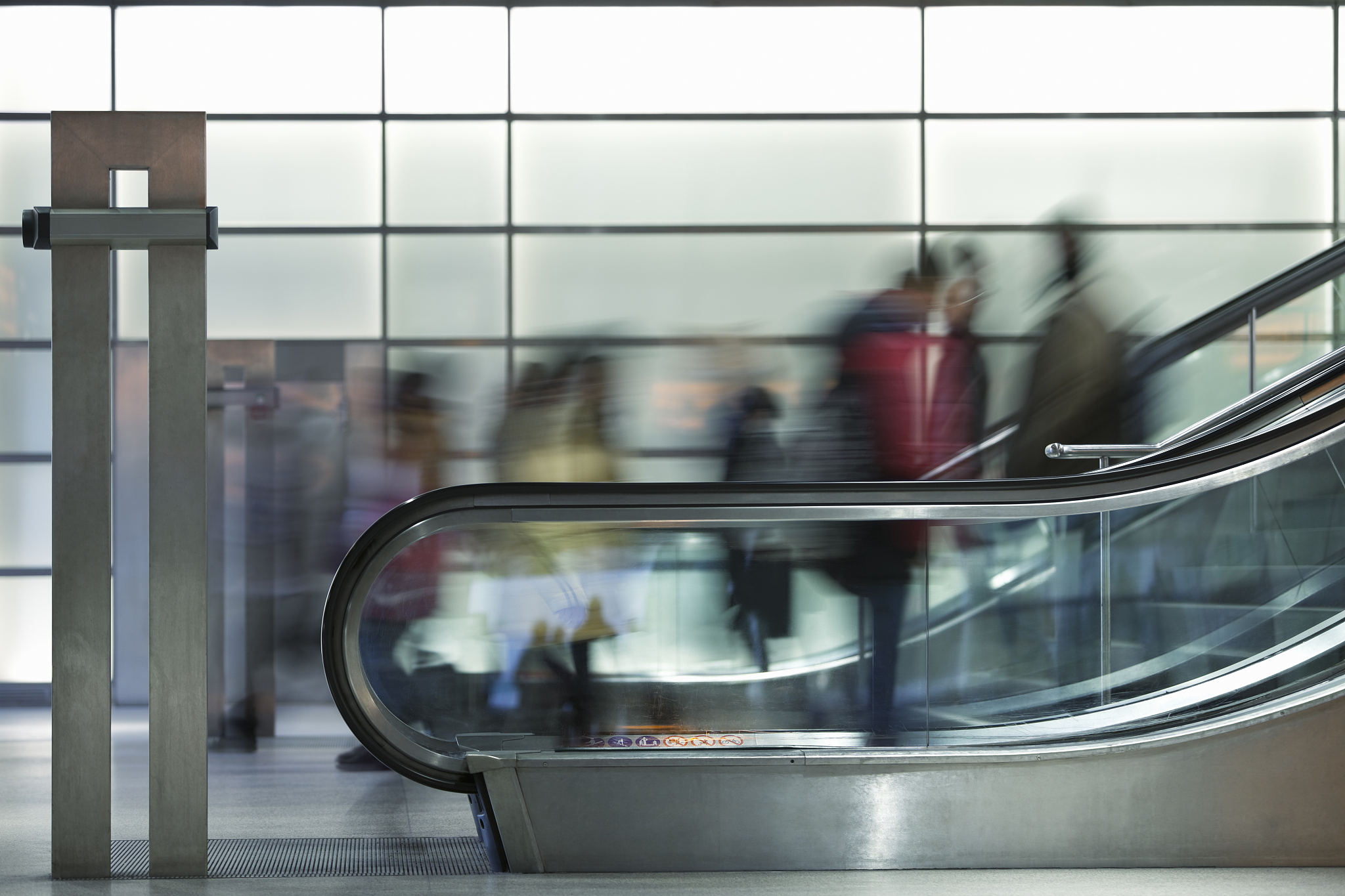 commuters on esclalators against illuminated glass wall, blurred