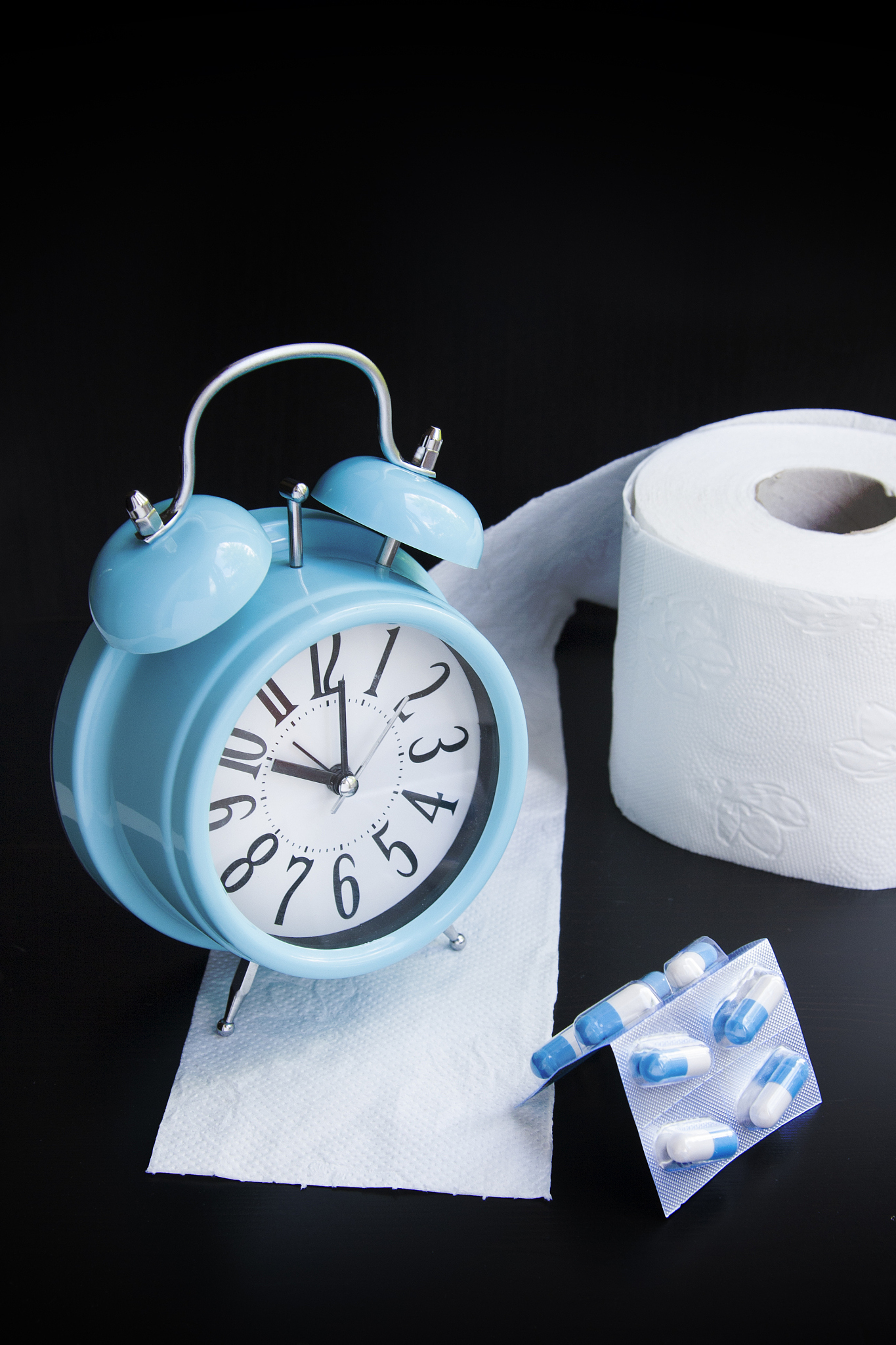 toilet paper, capsules and alarm clock on black