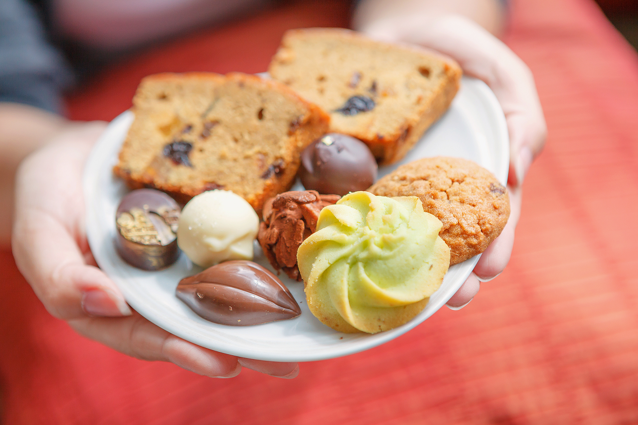 woman hands holding white plate of cookies, chocolate  and bread