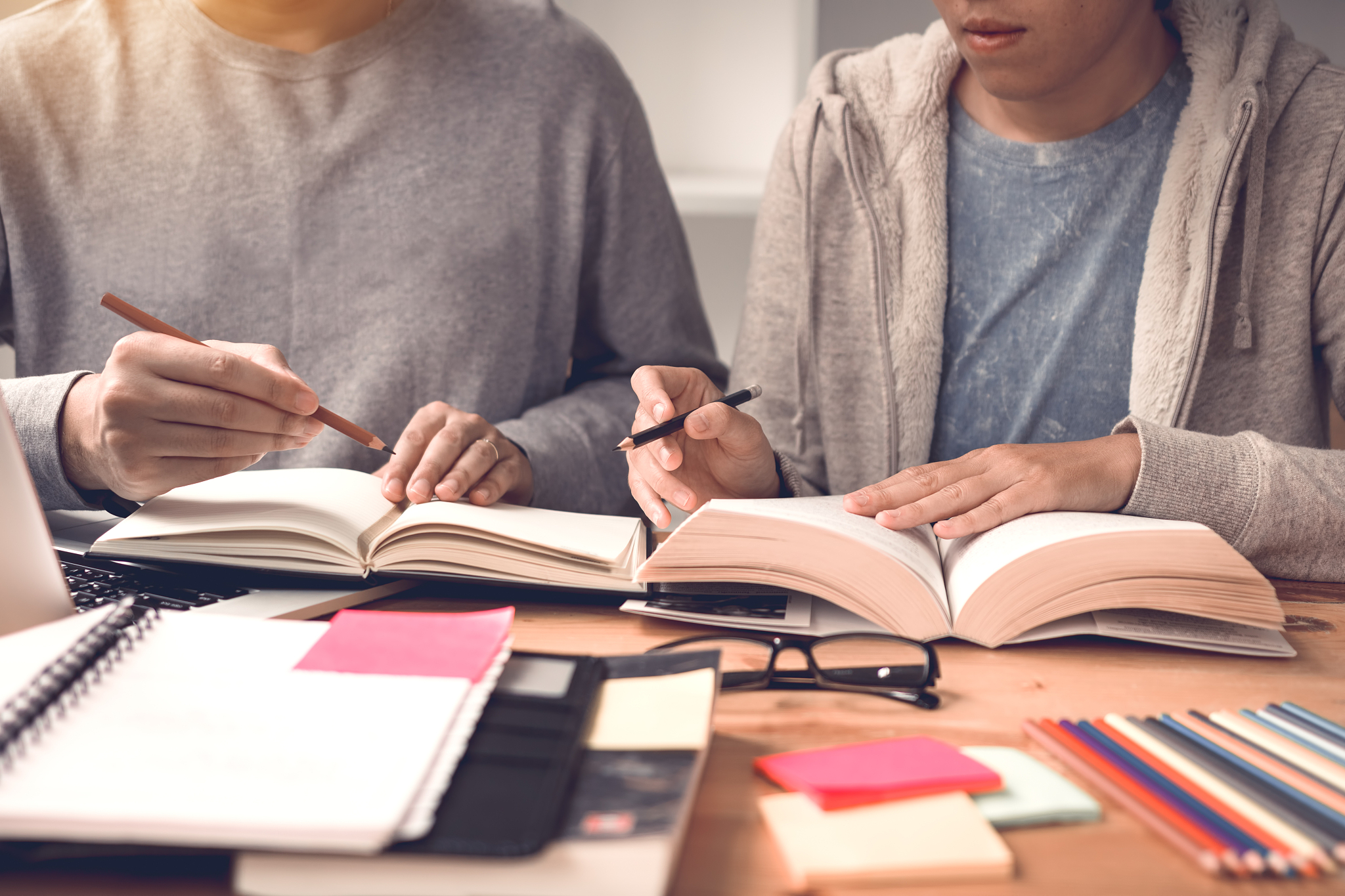 two student reading textbook for test together in library.
