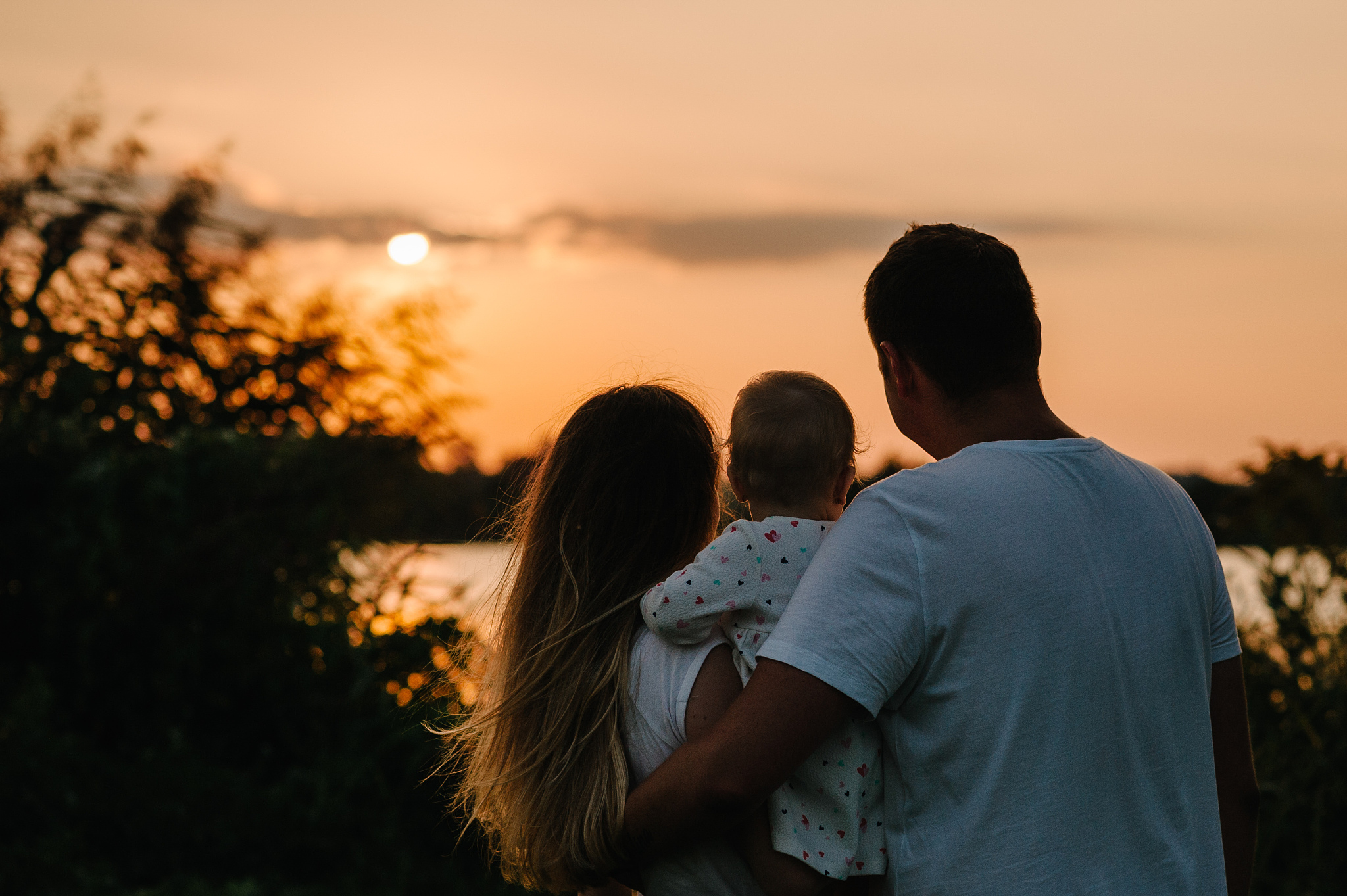 mom, dad holds daughter stand back and looking on sunset. portra