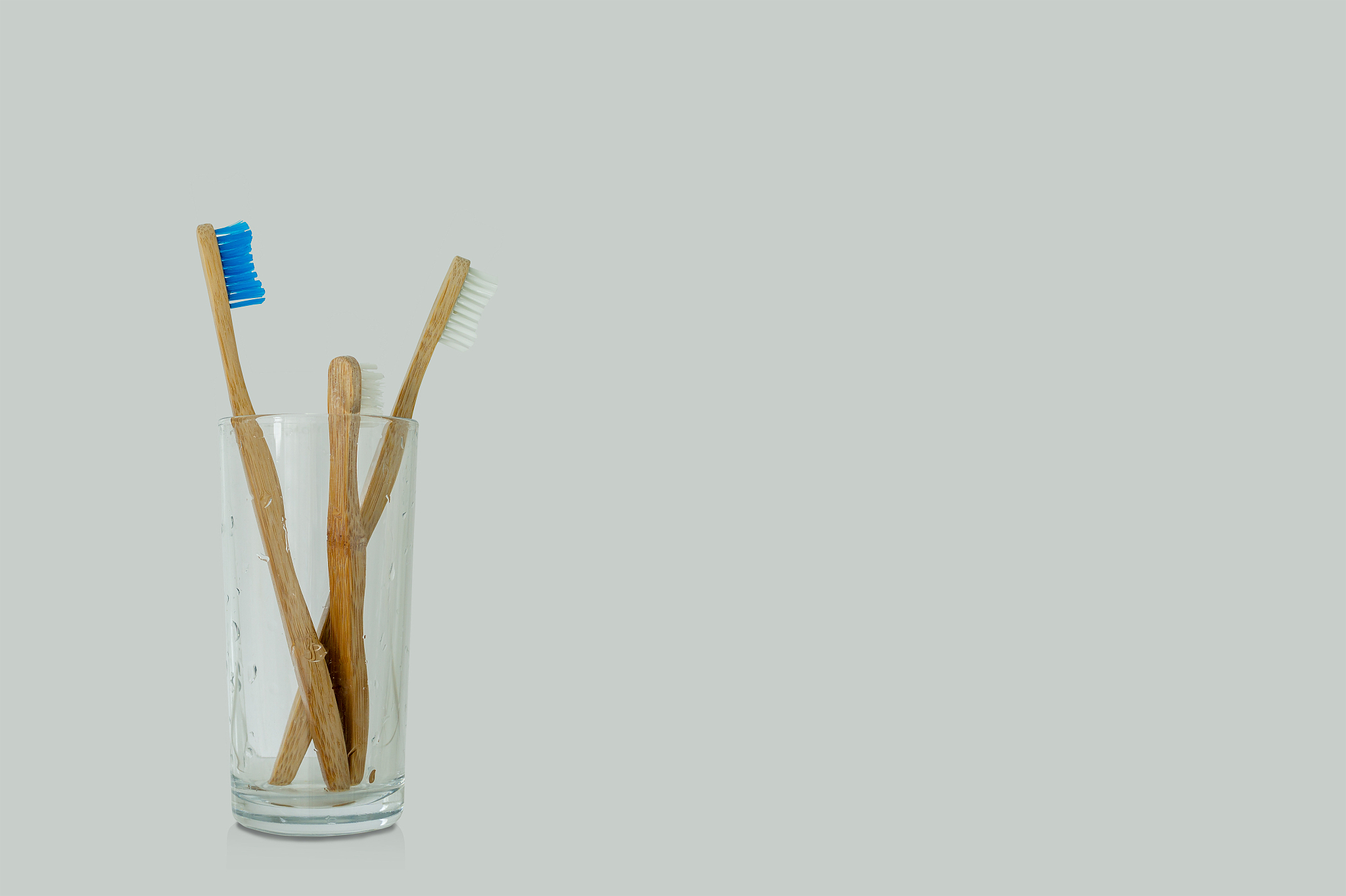 close up of three bamboo toothbrushes in a glass on a bright bac
