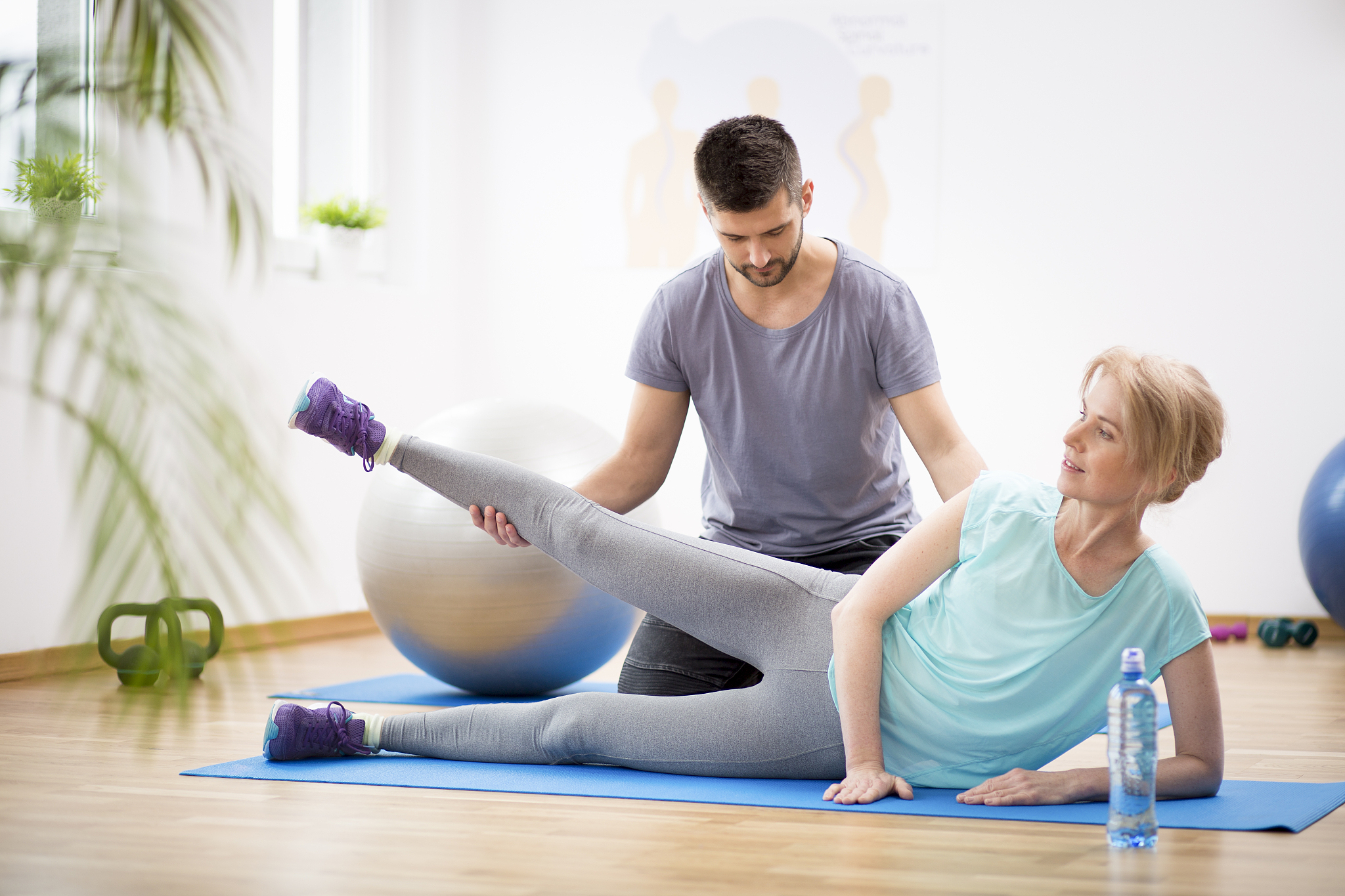 middle age woman exercising on blue mat during physiotherapy wit