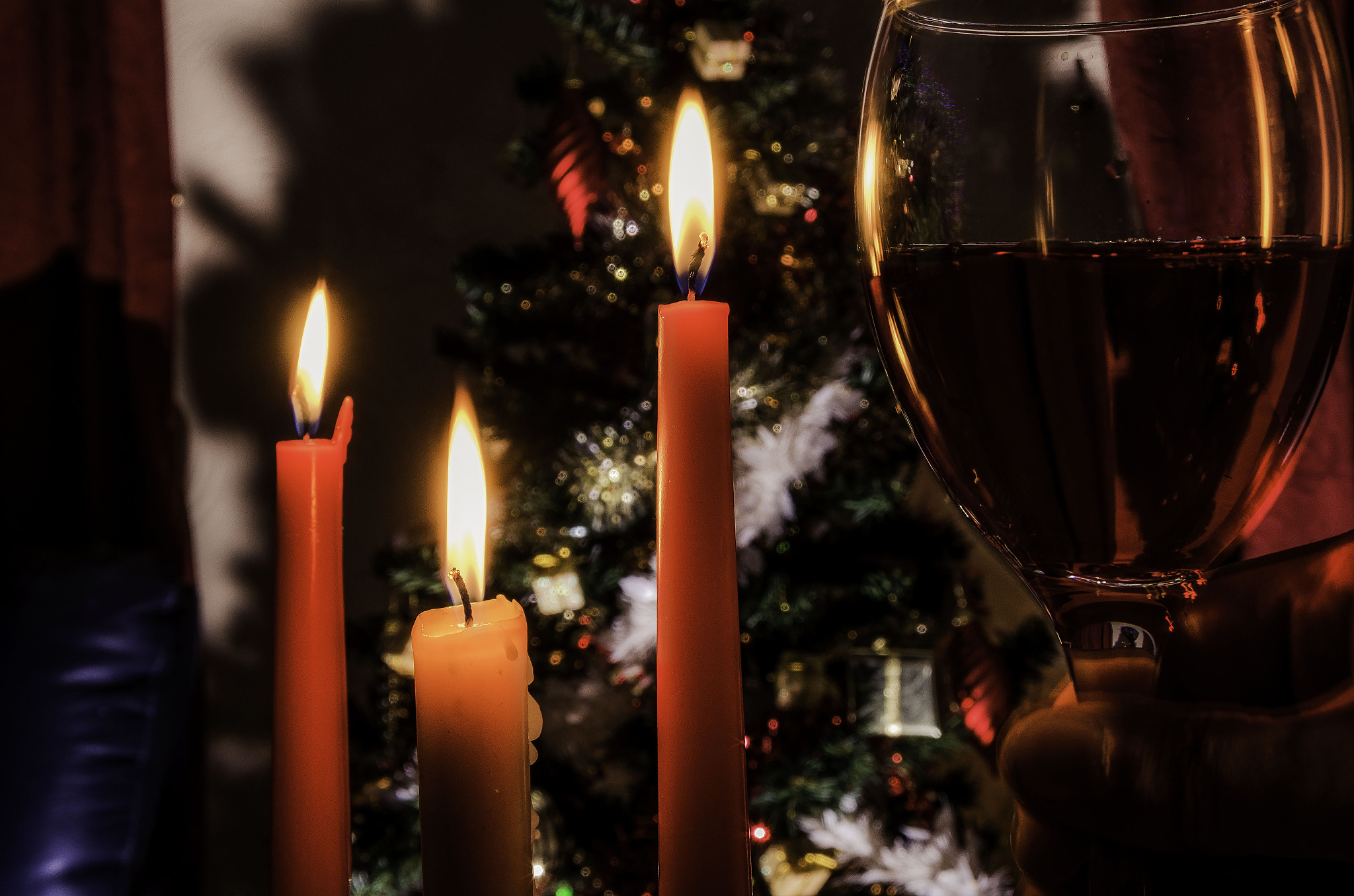 glass of red wine, three candles christmas tree in background