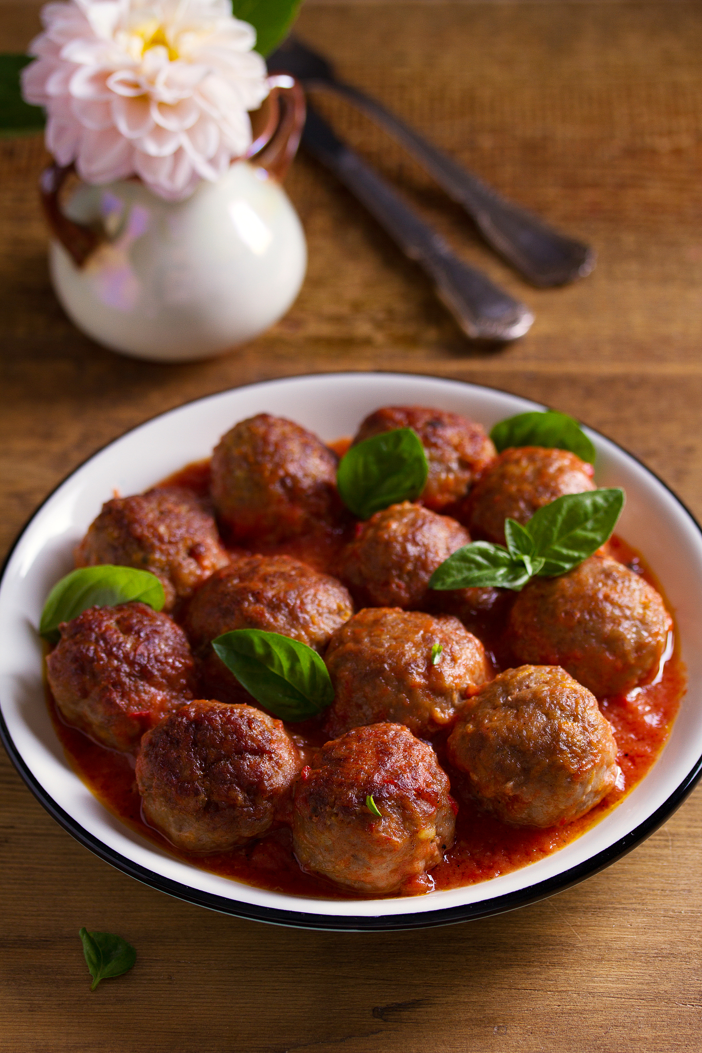 meatballs in tomato sauce, garnished with basil in bowl on woode
