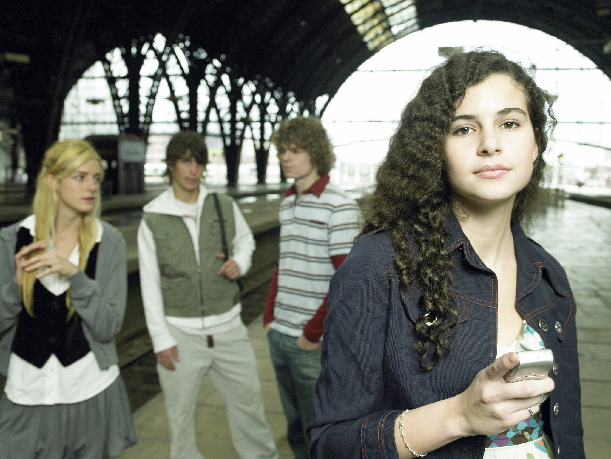 teenager holding cell phone, with friends at train station, wais