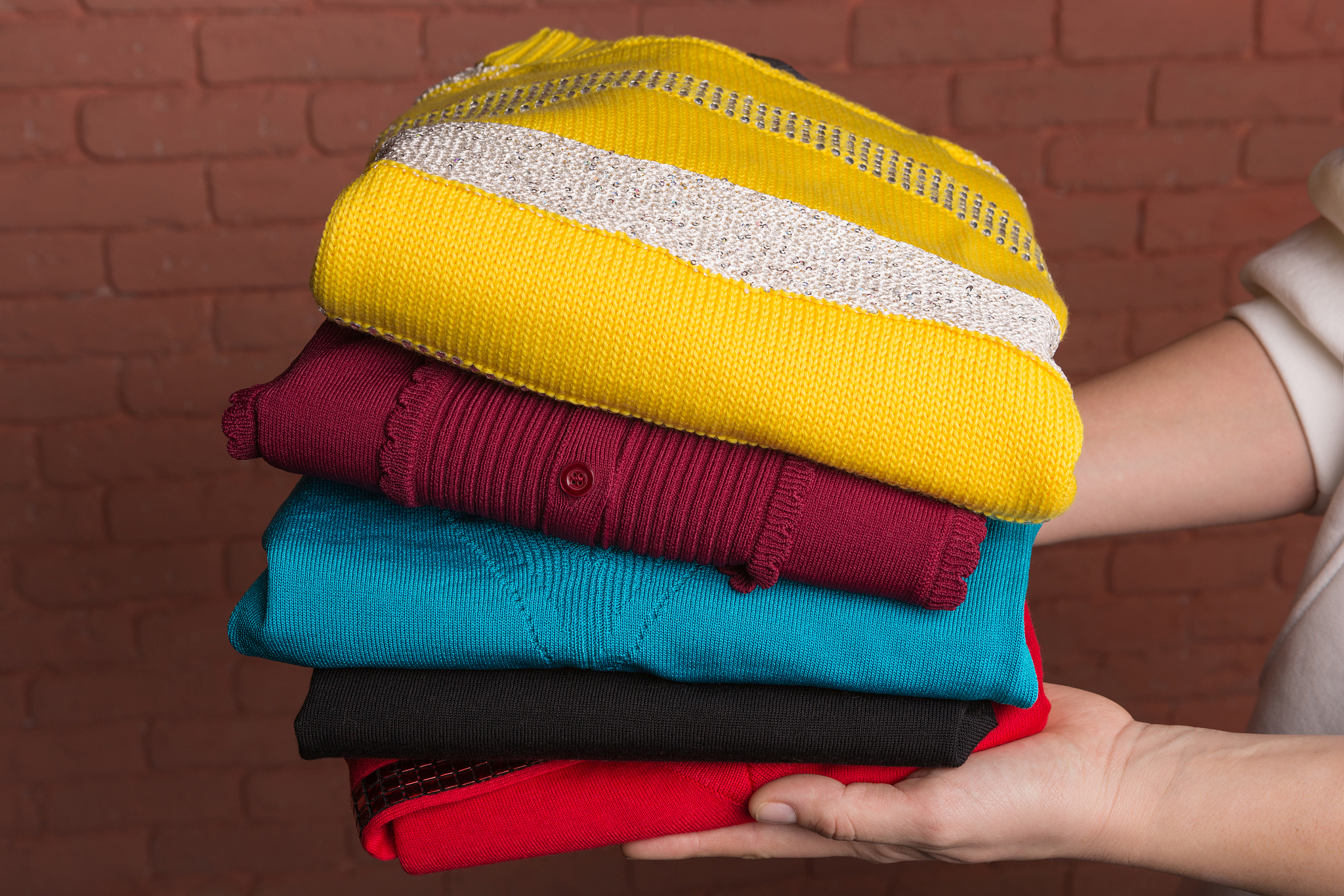 stack of female fashionable sweaters in female hands against a b