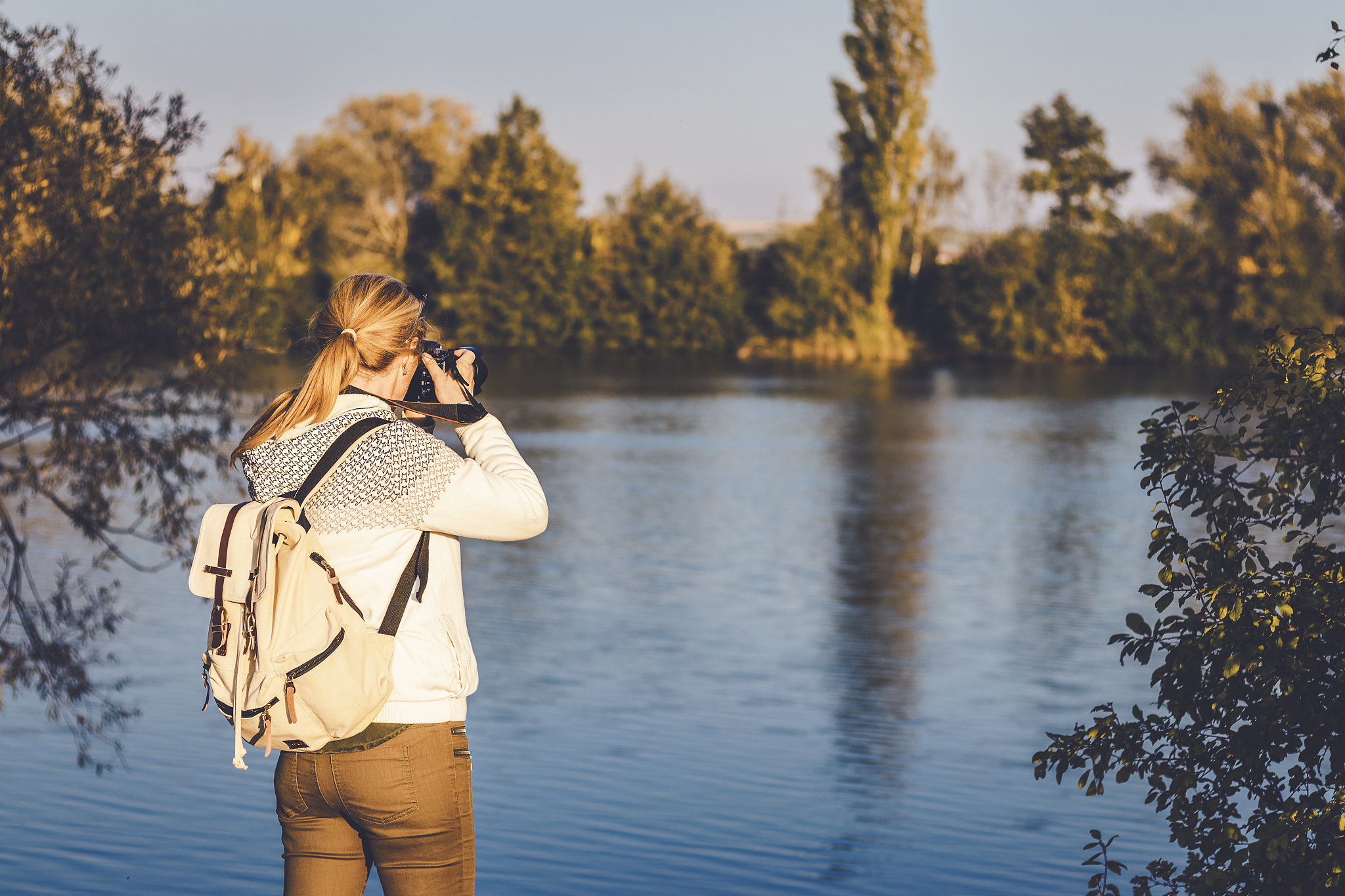 woman with backpack is photographing a landscape near to lake, t
