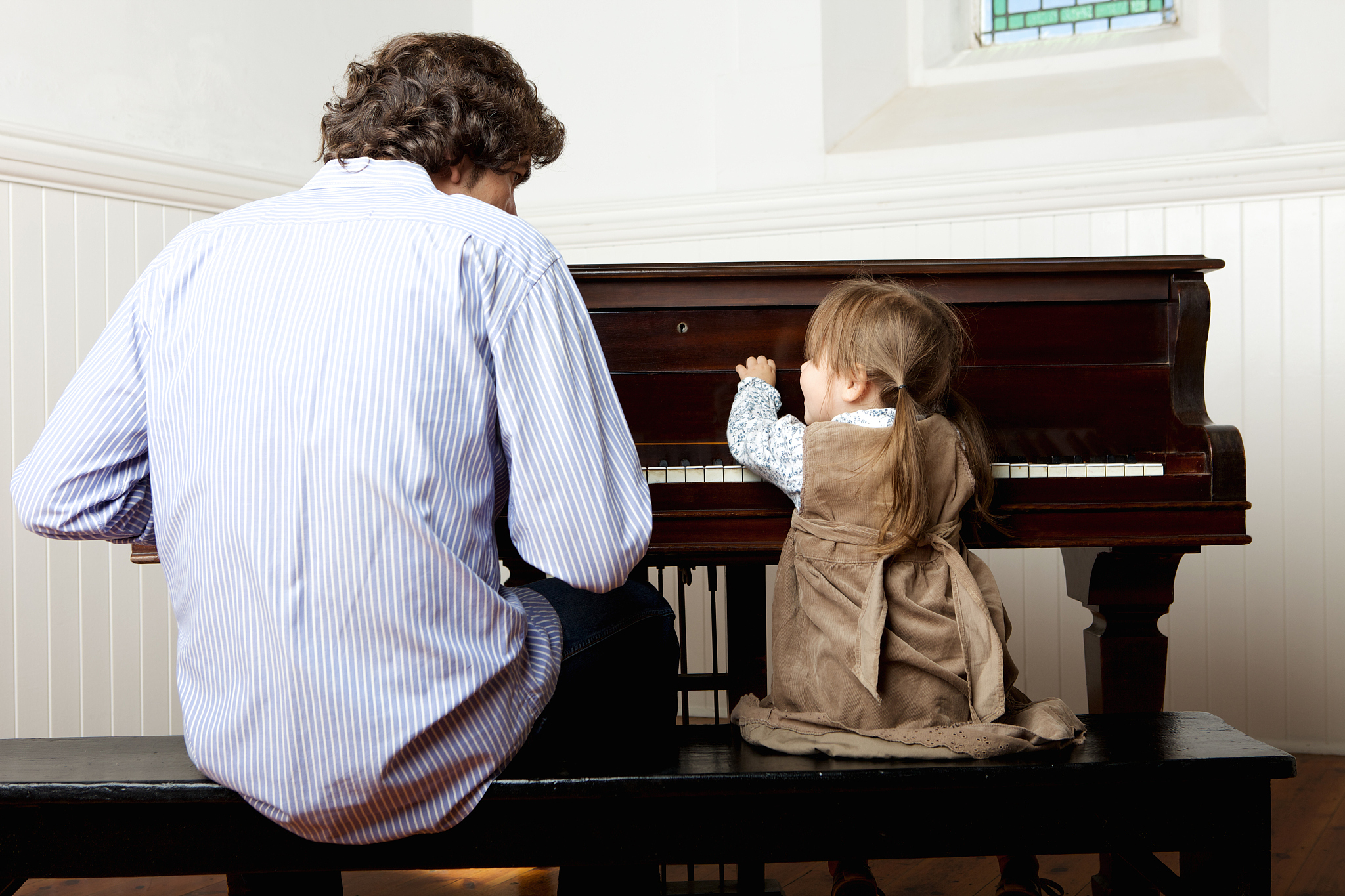 little girl playing the piano with father