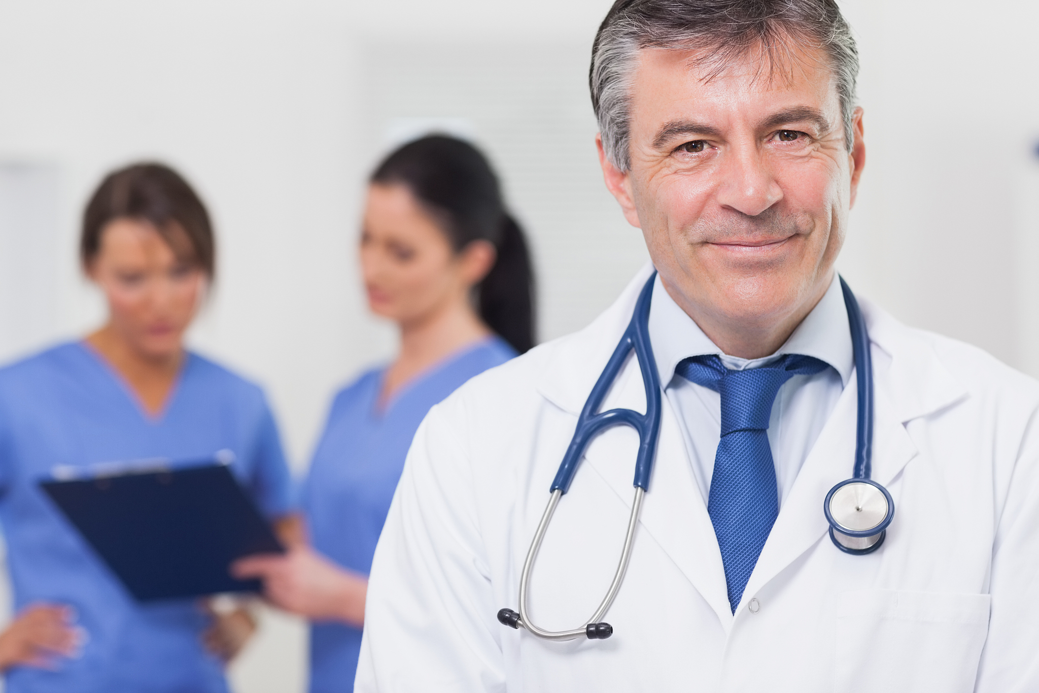 doctor with stethoscope smiling and his team behind him
