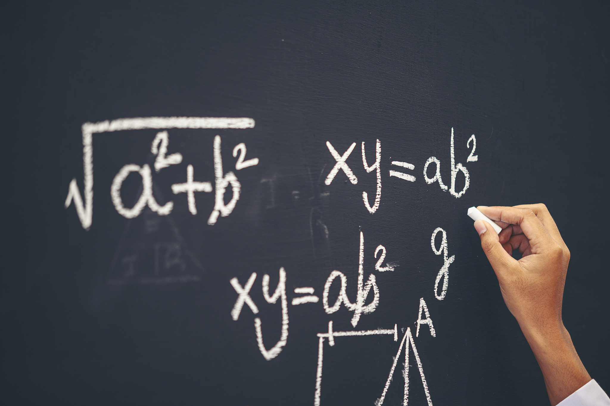 the hand that writes the formula with white chalk on the blackbo
