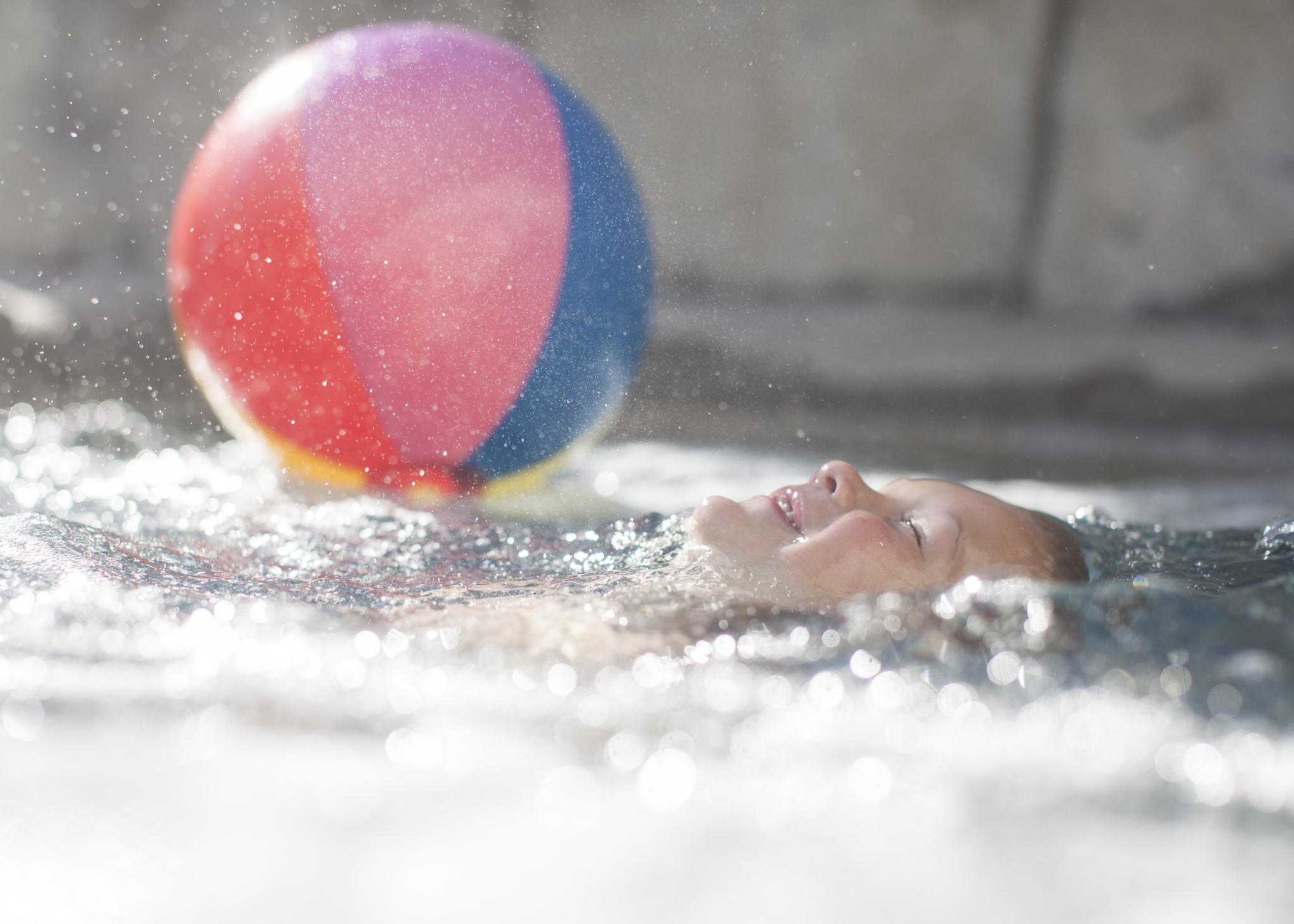 smiling boy floating in a swimming pool with a beach ball