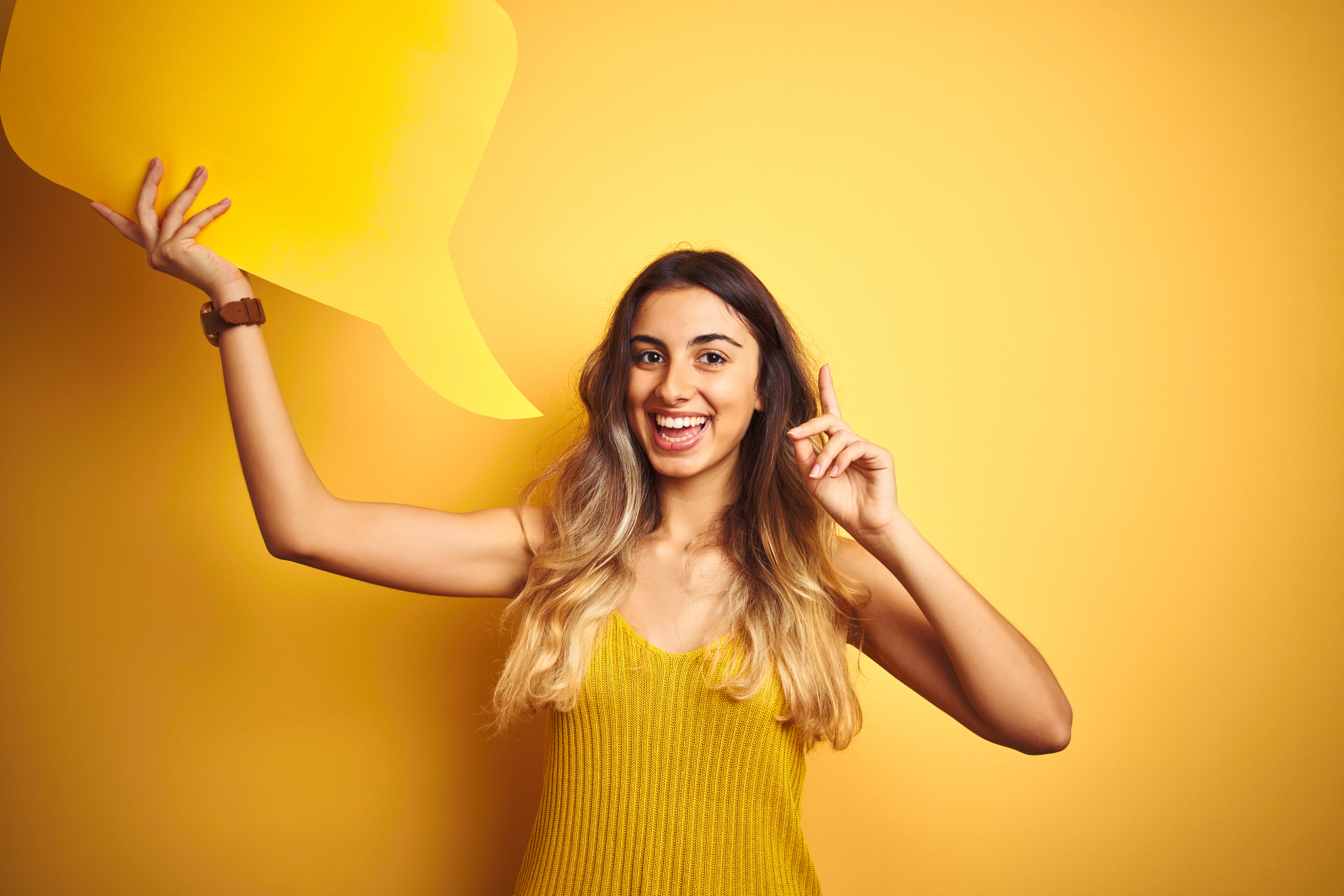 young beautiful woman holding speech bubble over yellow isolated