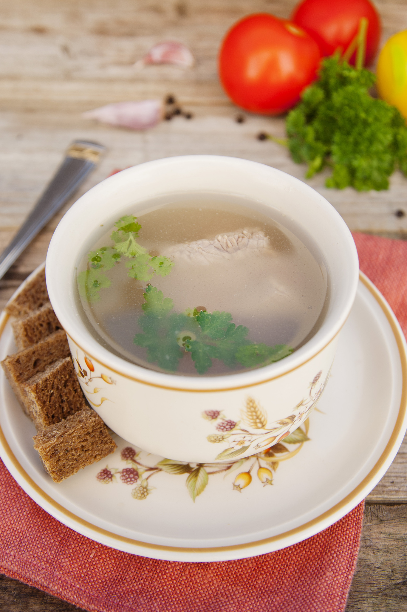 clear beef broth, bouillon in white bowl and vegetables on woode