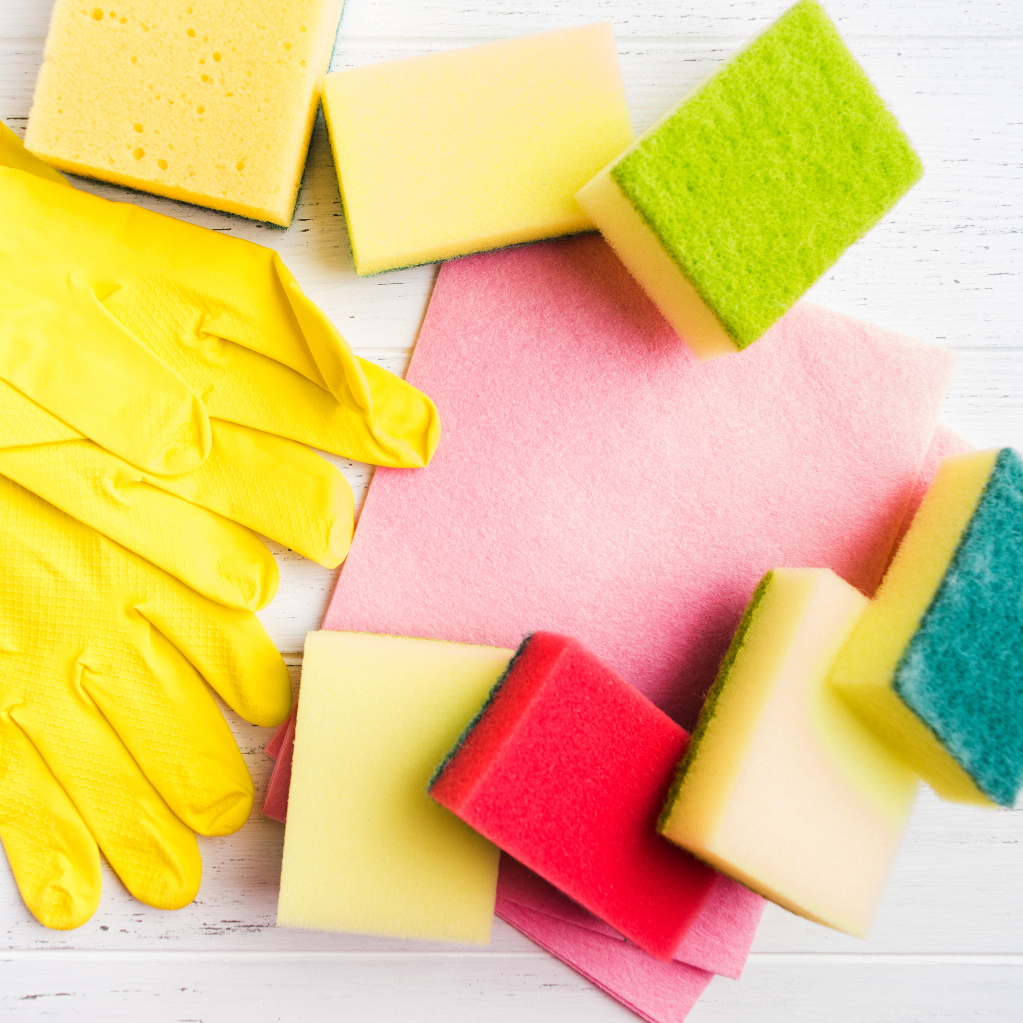 sponges, washcloth, rubber gloves on white wooden table with cop