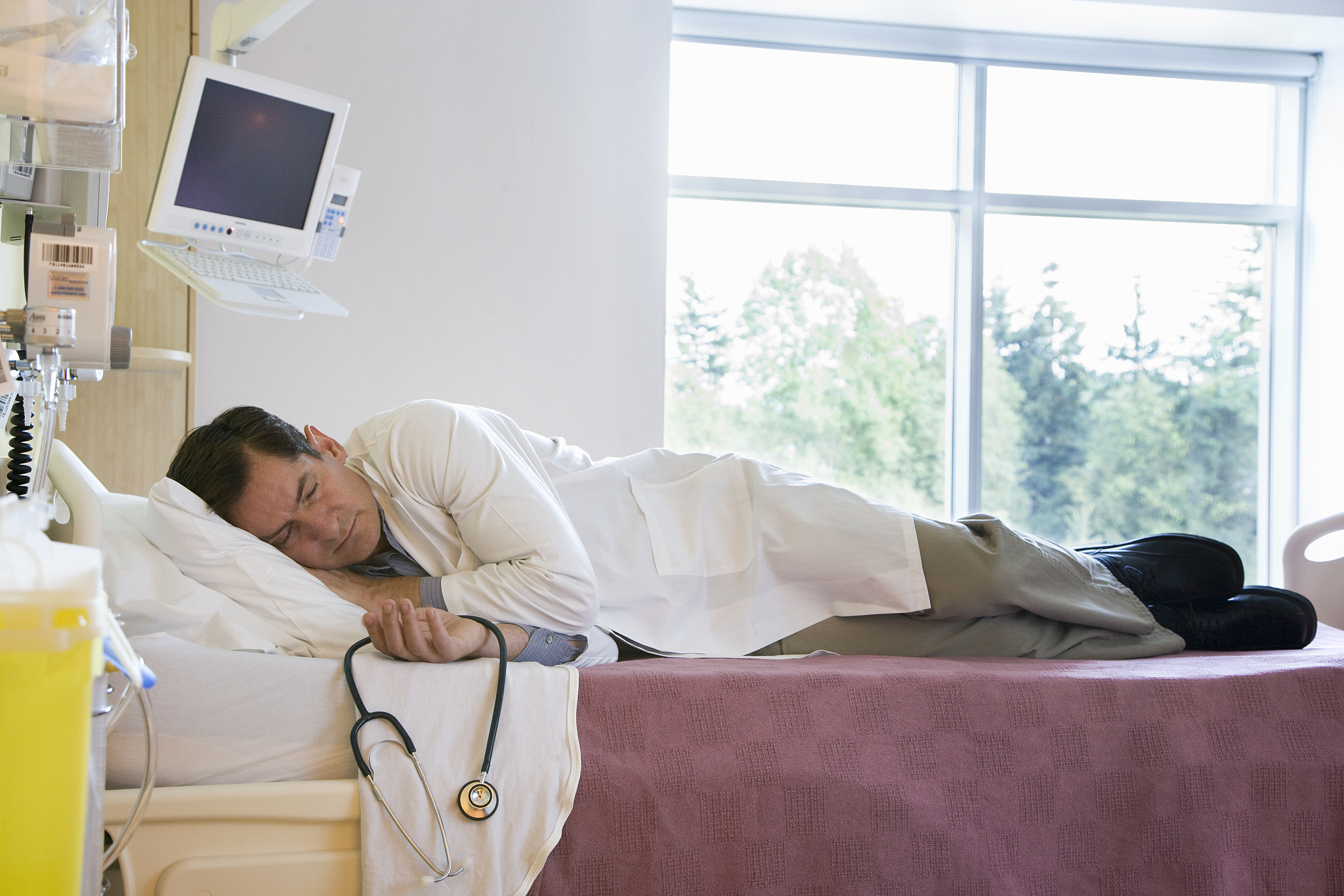 exhausted doctor sleeping in patients bed
