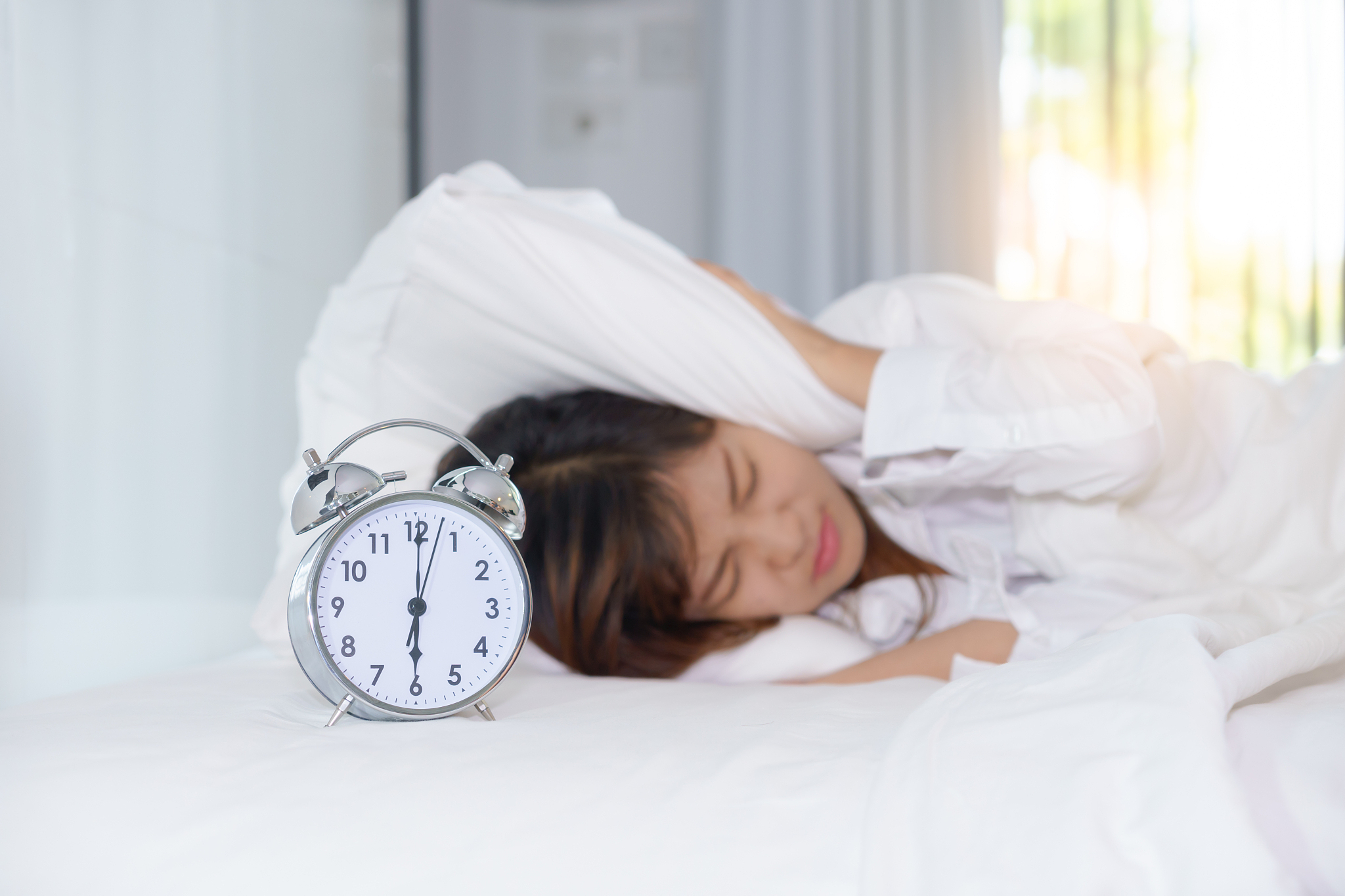 sleepy young woman woken up by alarm clock and hands covering he