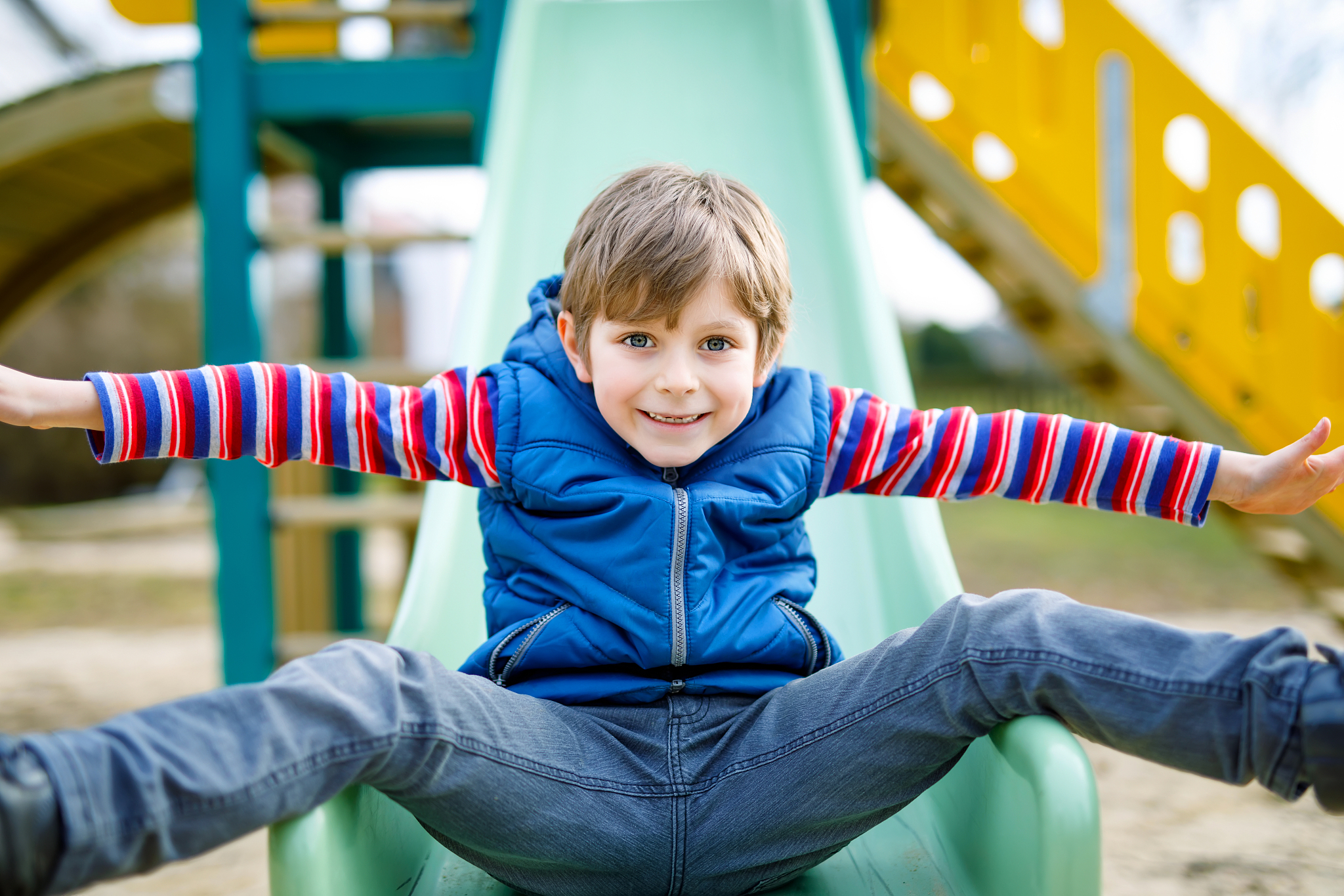happy blond kid boy having fun and sliding on outdoor playground