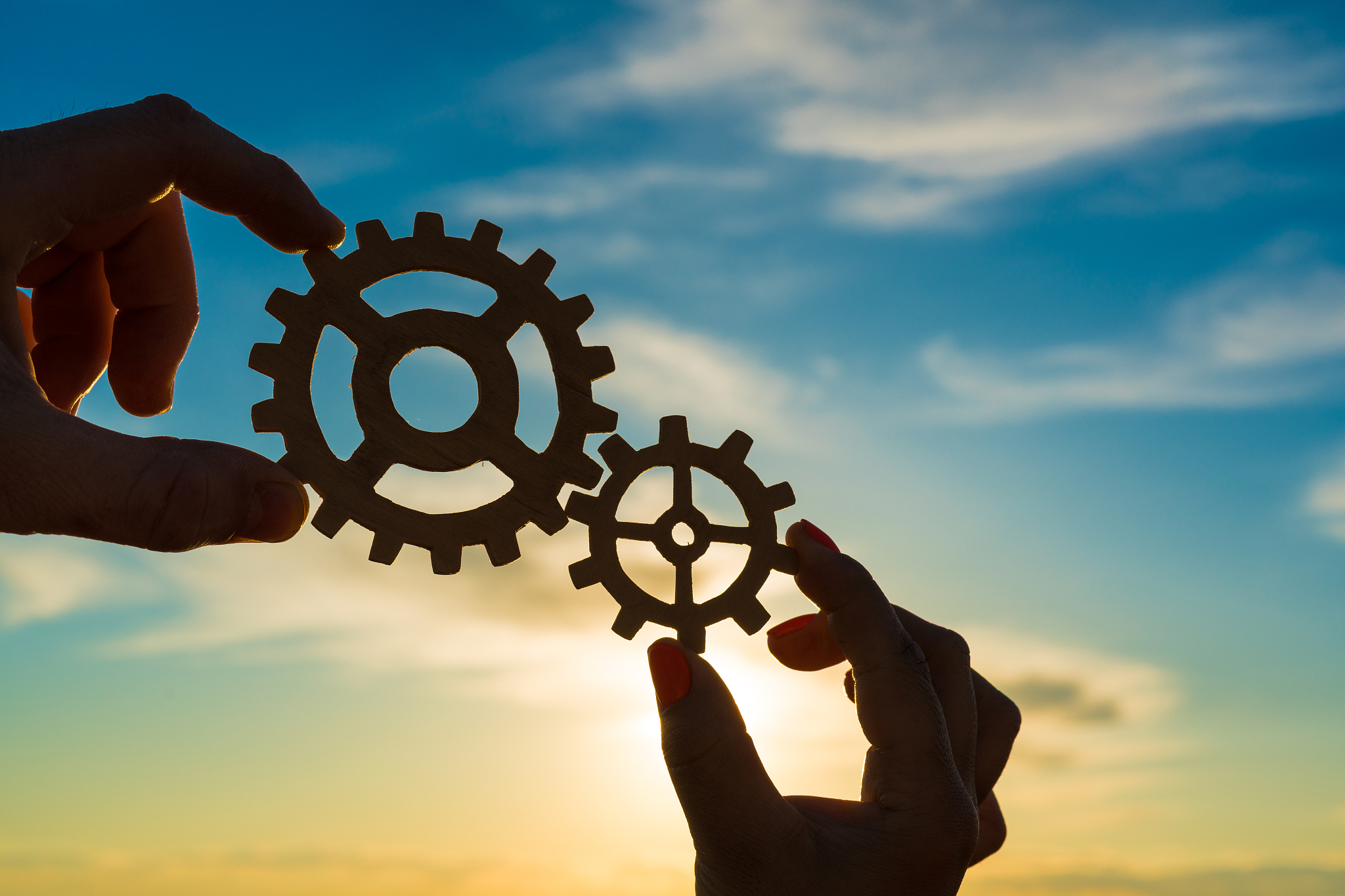 two hands of businessmen connect gears to a puzzle on a sunset b