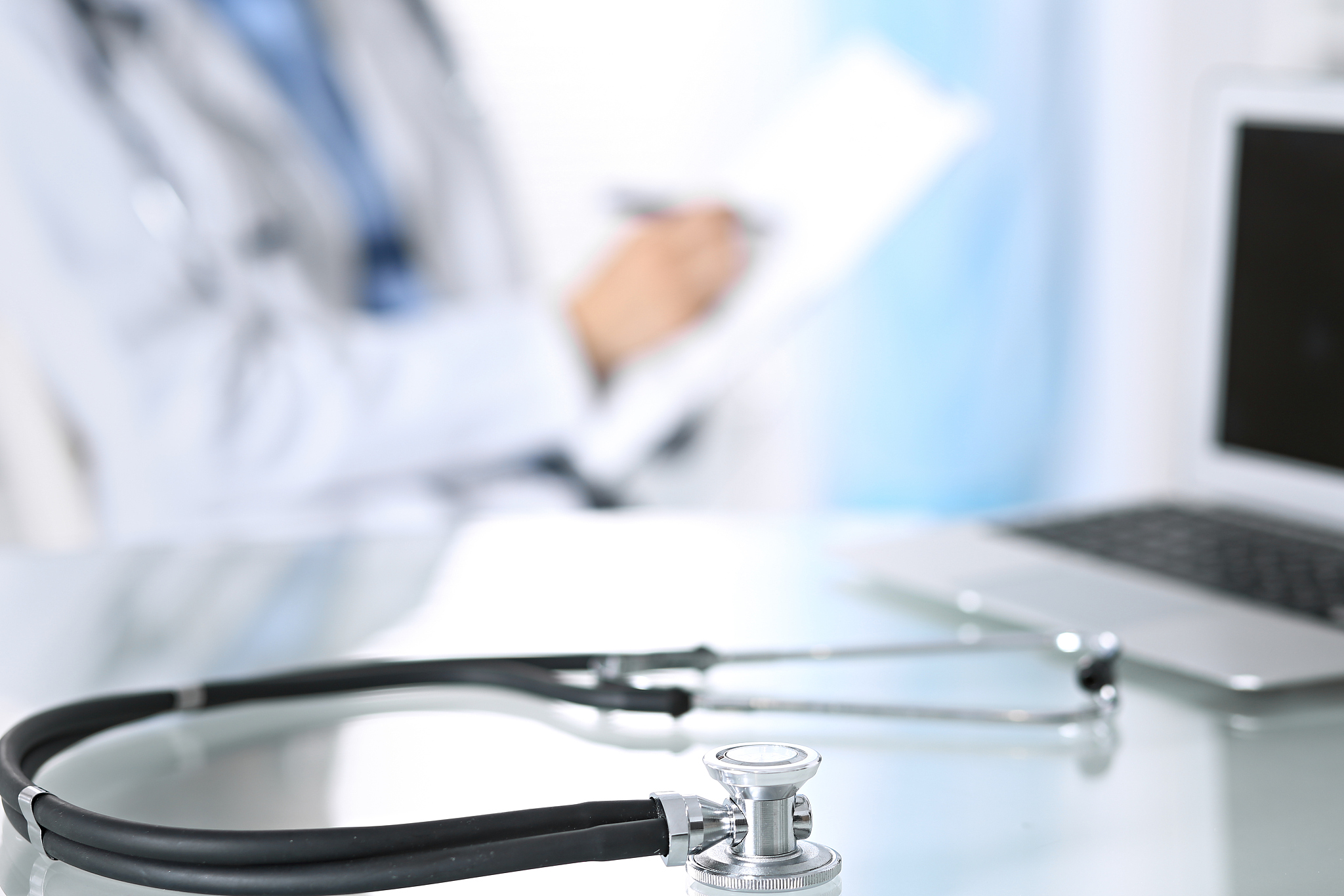stethoscope lying on glass desk with laptop computer at busy phy