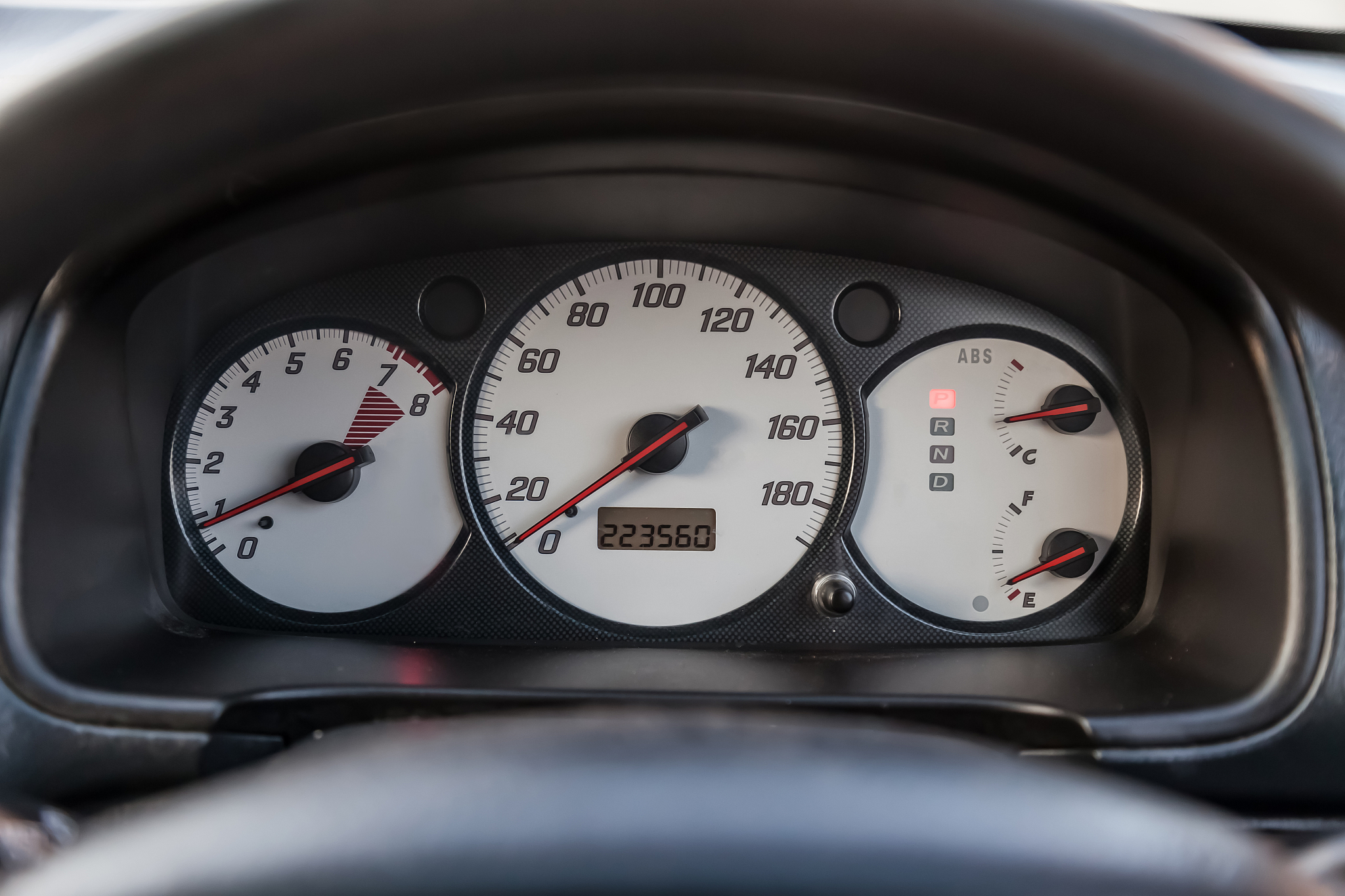car dashboard with white dials and red arrows on the speedometer